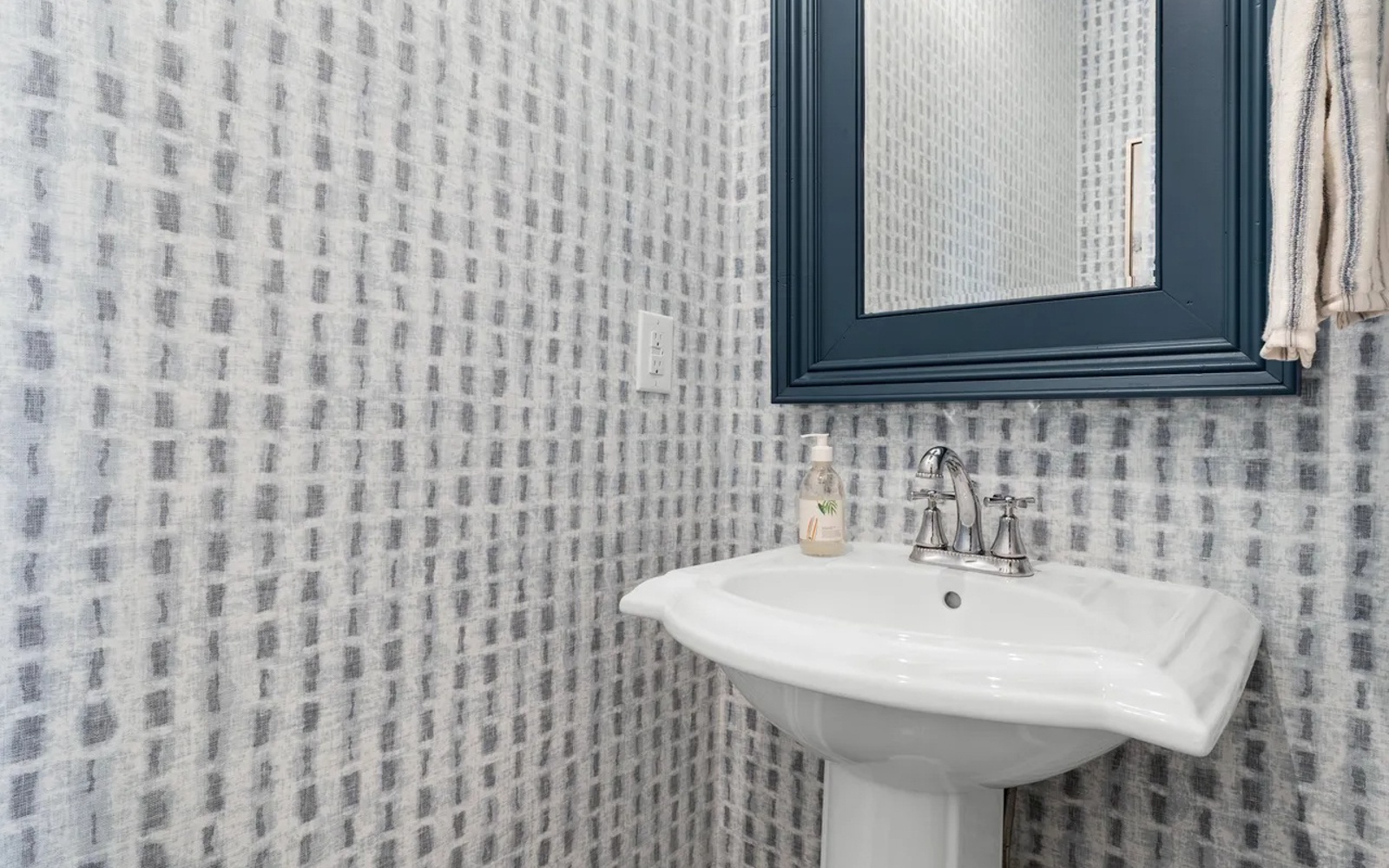 Step into your stylish powder room featuring geometric wallpaper and a classic pedestal sink with polished chrome fixtures.