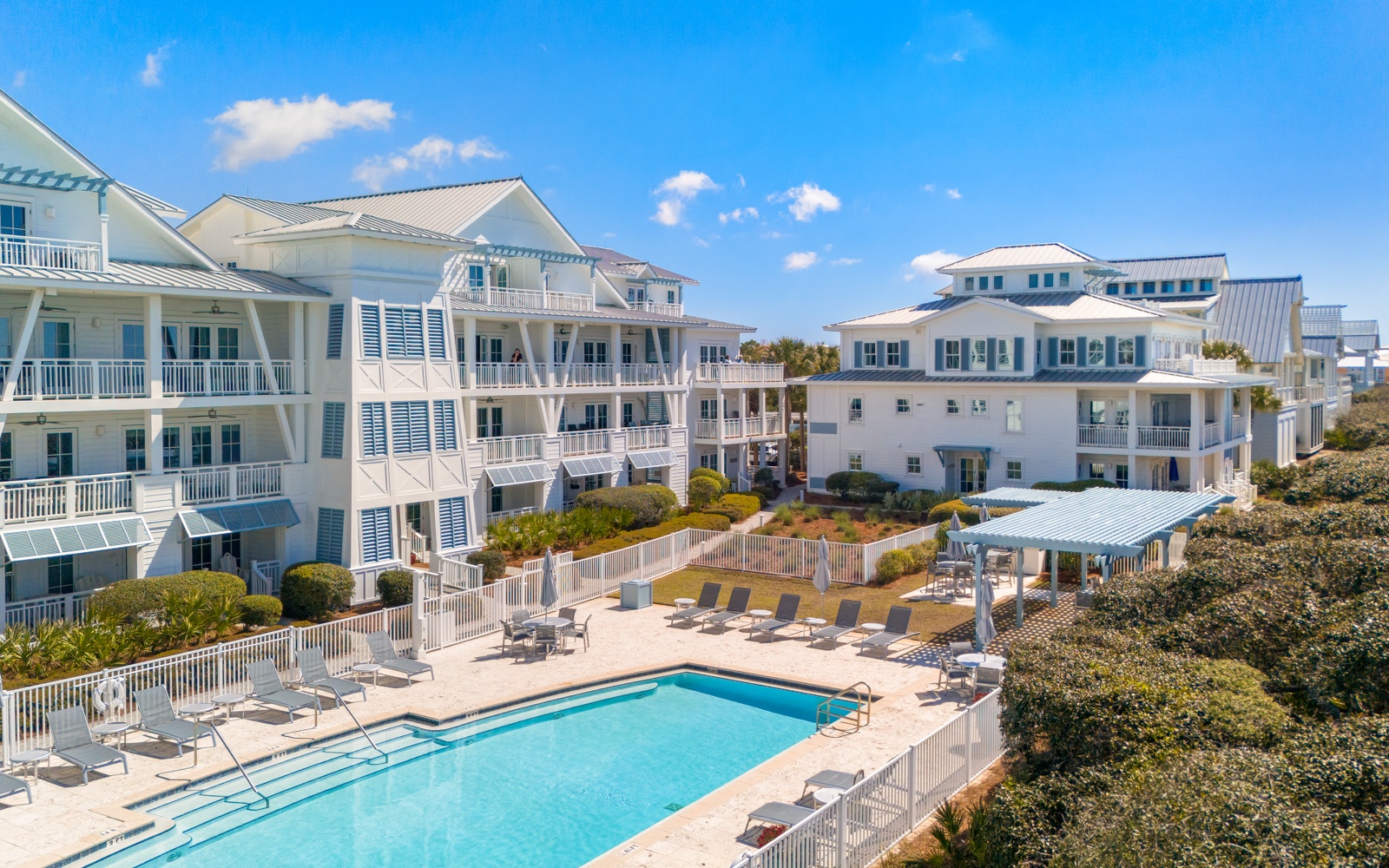Coastal vacation buildings with swimming pool and outdoor spaces surrounded by tropical landscaping under bright blue skies.