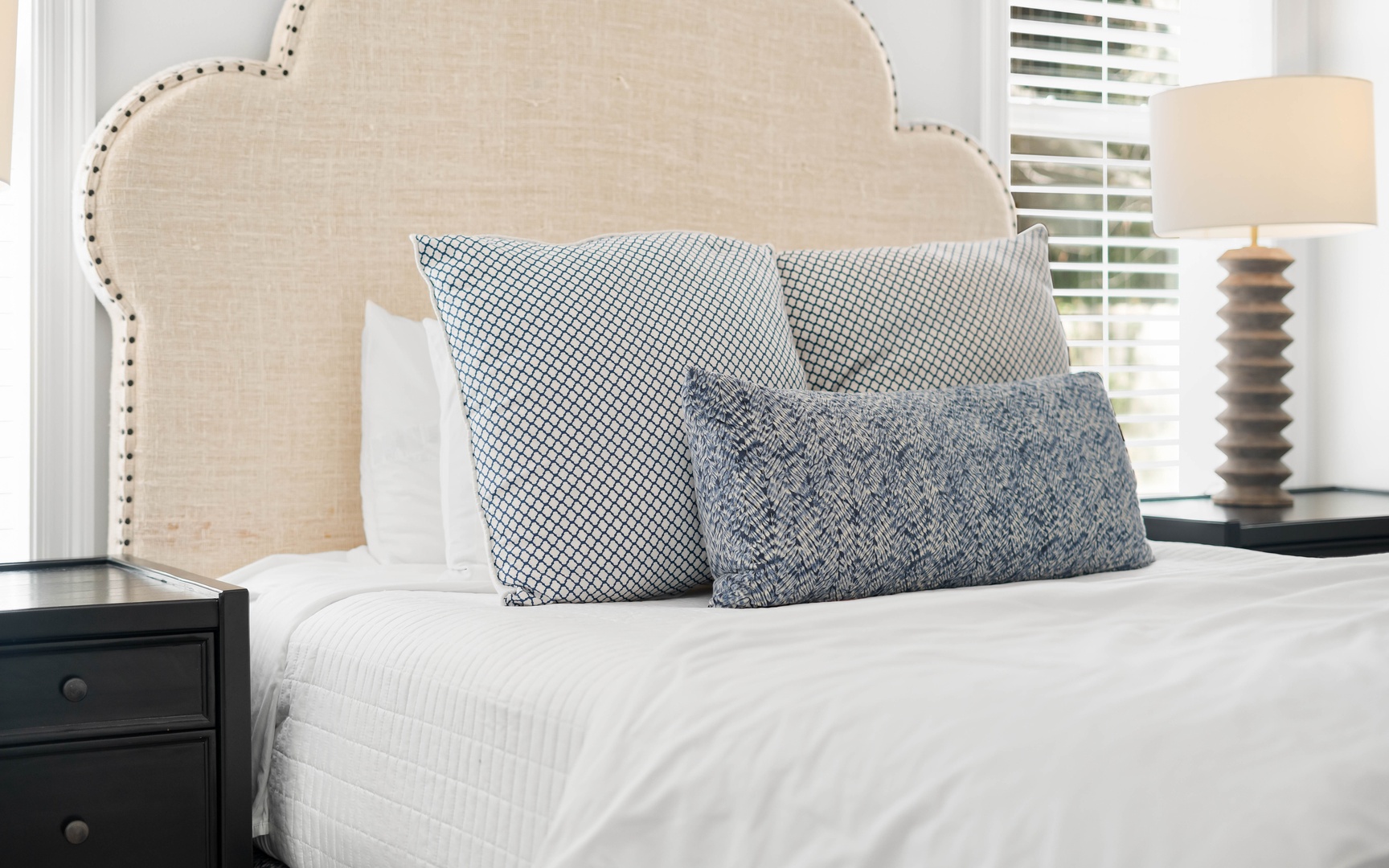 Sink into this serene bedroom where crisp white linens meet stylish patterned pillows, creating your perfect retreat for restful nights.