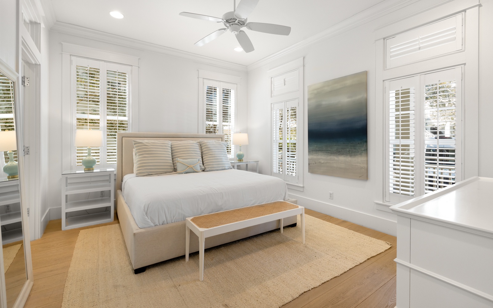 Unwind in your serene coastal bedroom with calming artwork and natural light streaming through shuttered windows.