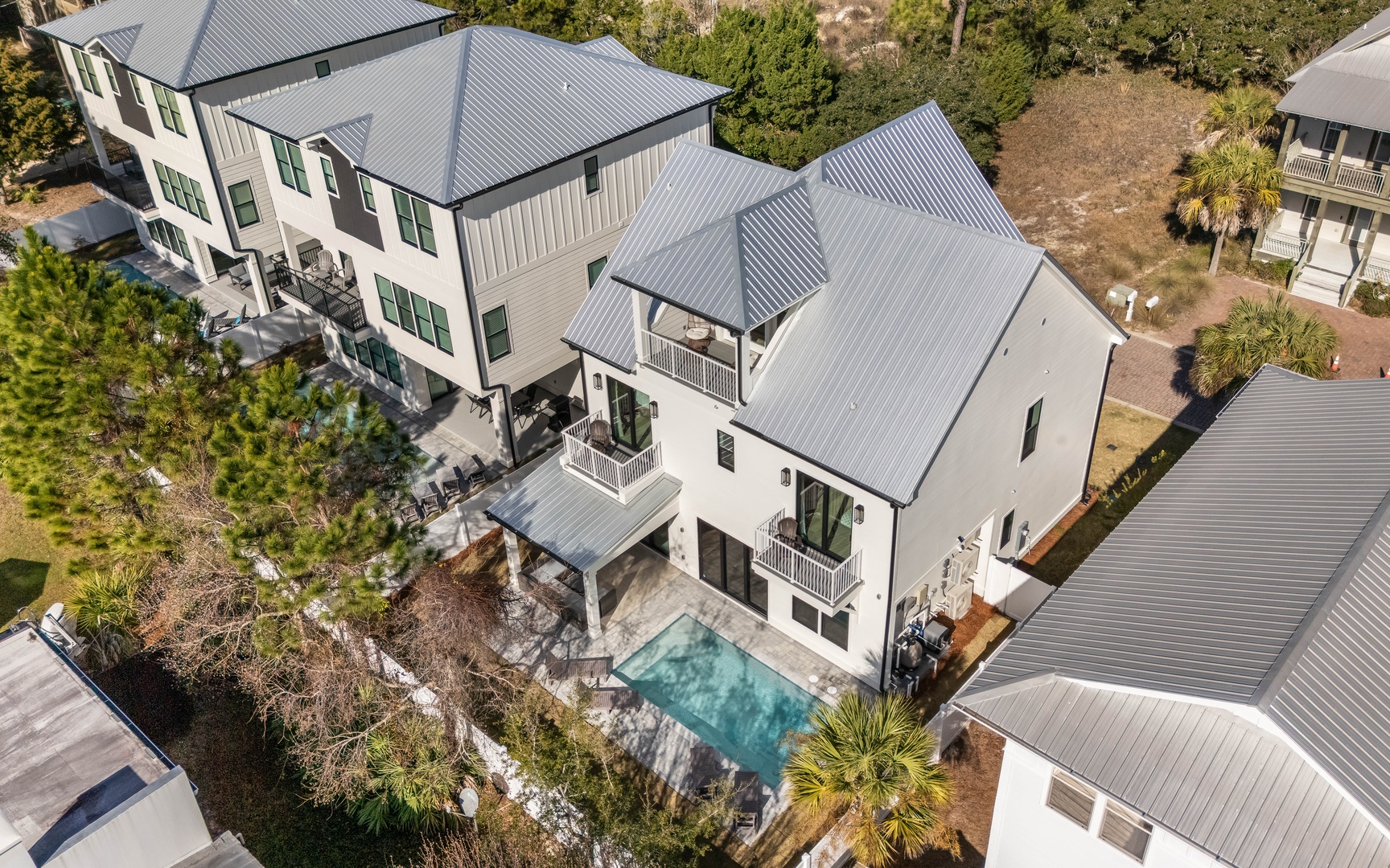 Stunning modern coastal home featuring elegant white exterior, multiple levels with balconies, private swimming pool, and lush landscaping in peaceful neighborhood setting.