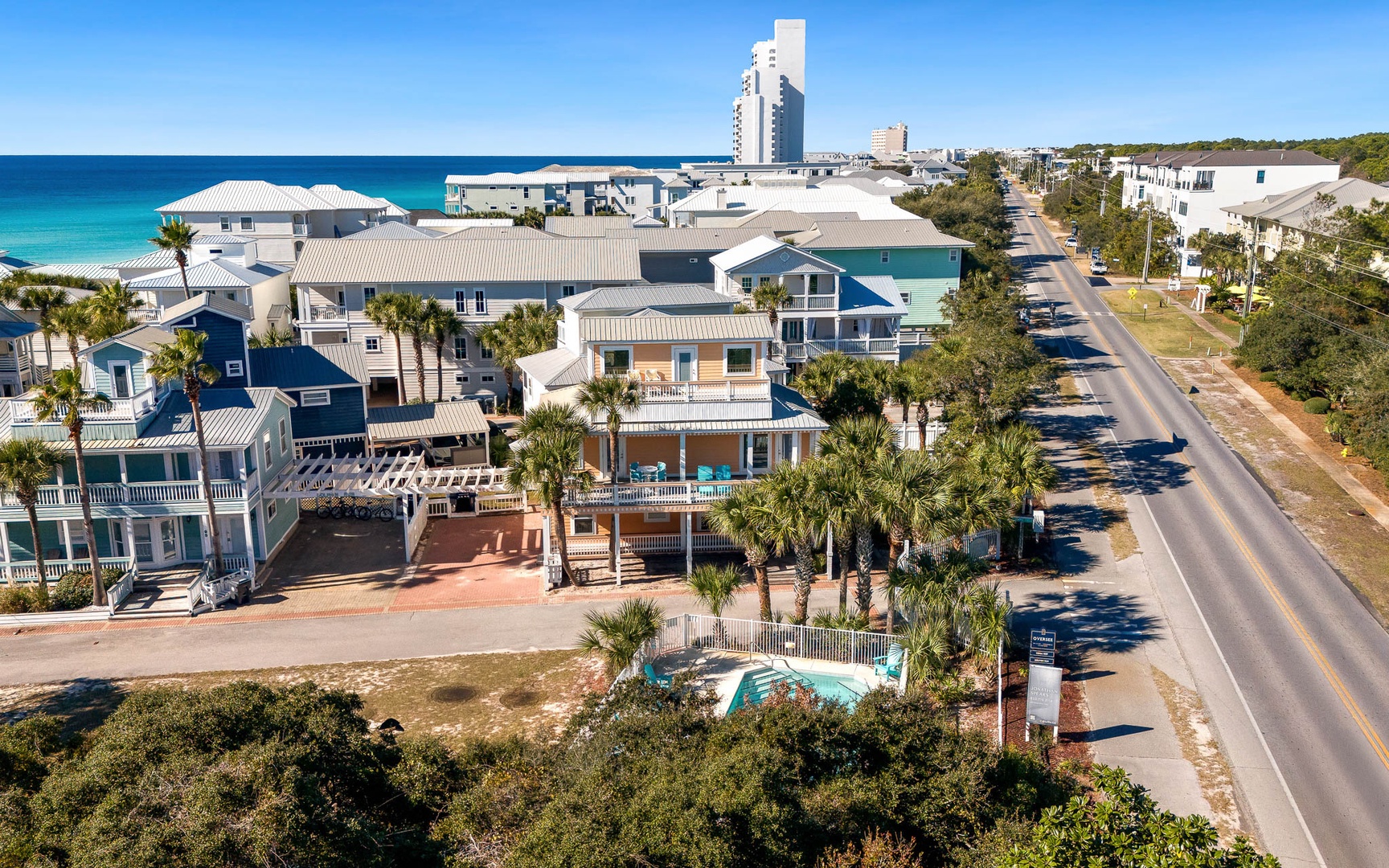 Aerial view of colorful beachfront vacation homes along a coastal road, with pristine turquoise waters and white sand beaches nearby.