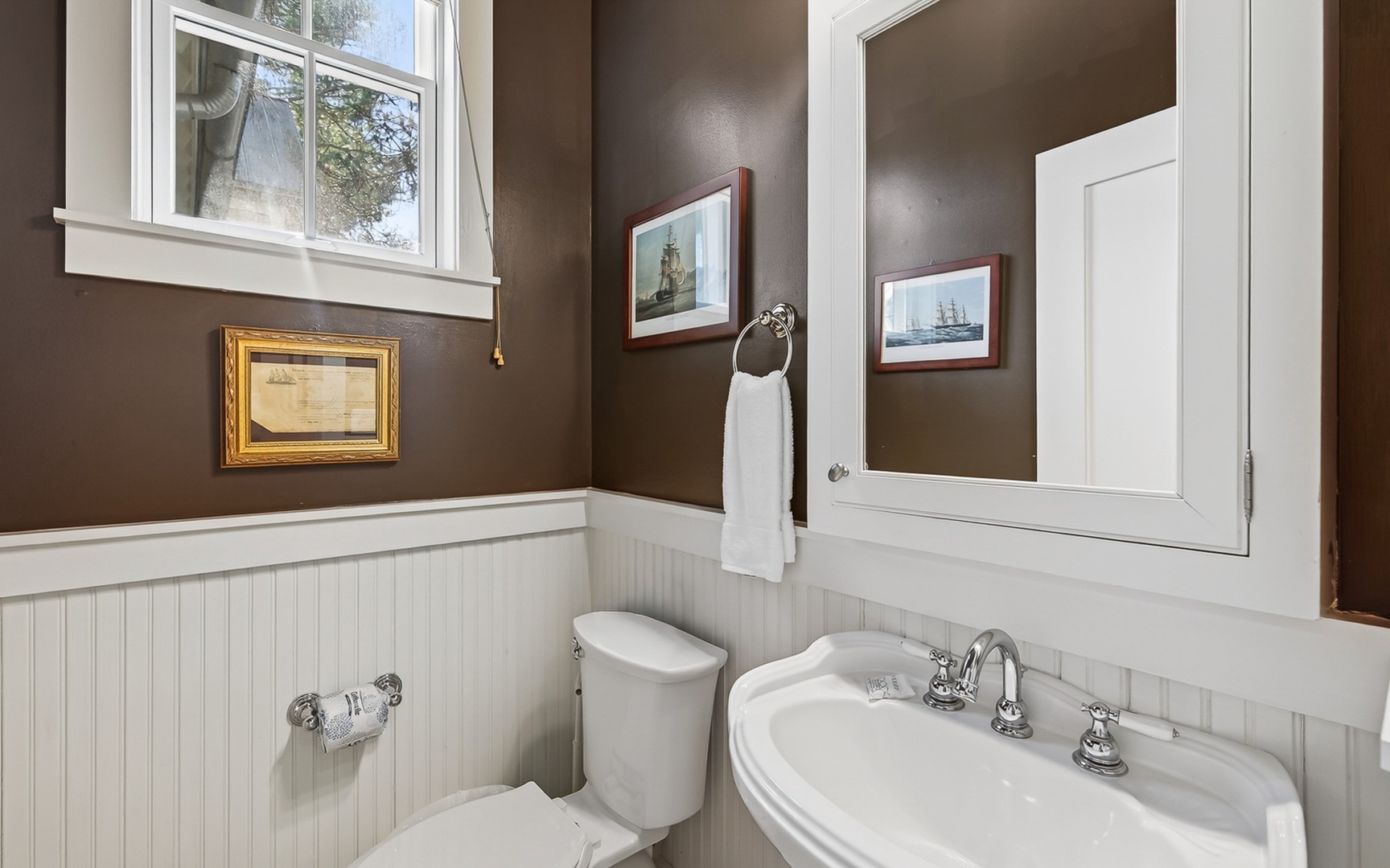 Step into your charming bathroom with classic wainscoting, nautical artwork, and a crisp white vanity that creates the perfect coastal retreat.