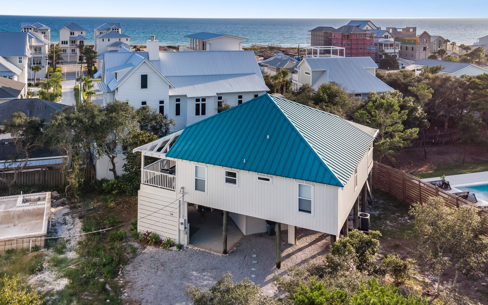 Charming coastal cottage with distinctive turquoise roof nestled among beach homes just steps from the shoreline.