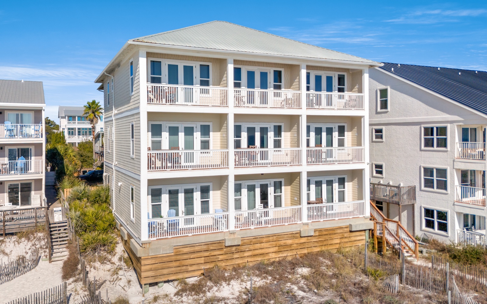 Coastal vacation home featuring multiple balconies and bright windows, situated steps from sandy beaches with natural dune vegetation.