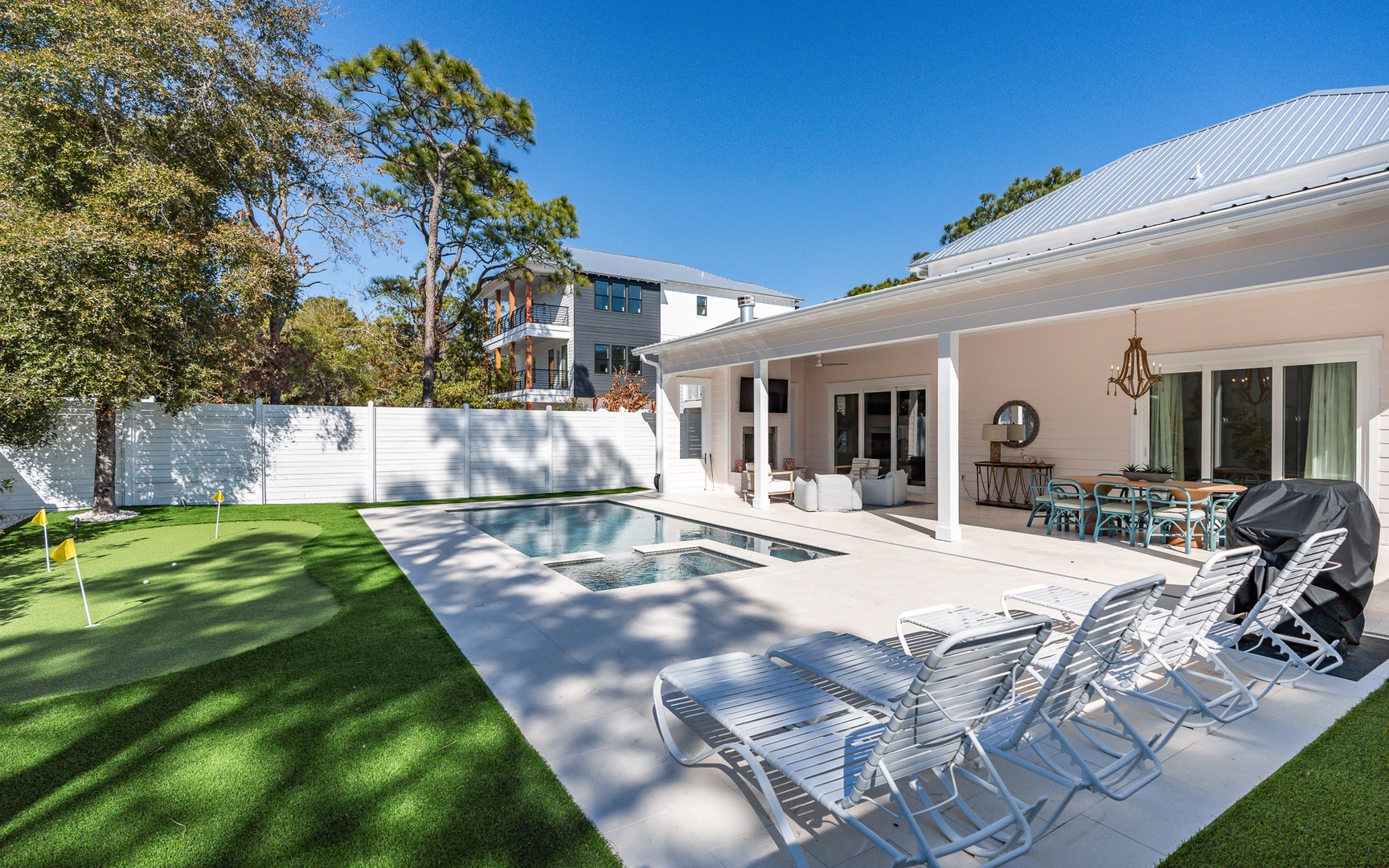 Modern property featuring pristine pool area, covered patio with dining space, and lush landscaping under clear blue skies.