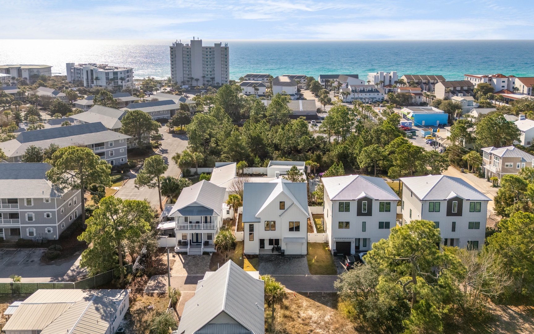 Aerial view of coastal vacation rental properties nestled among mature trees, just steps from pristine turquoise waters and white sand beaches.
