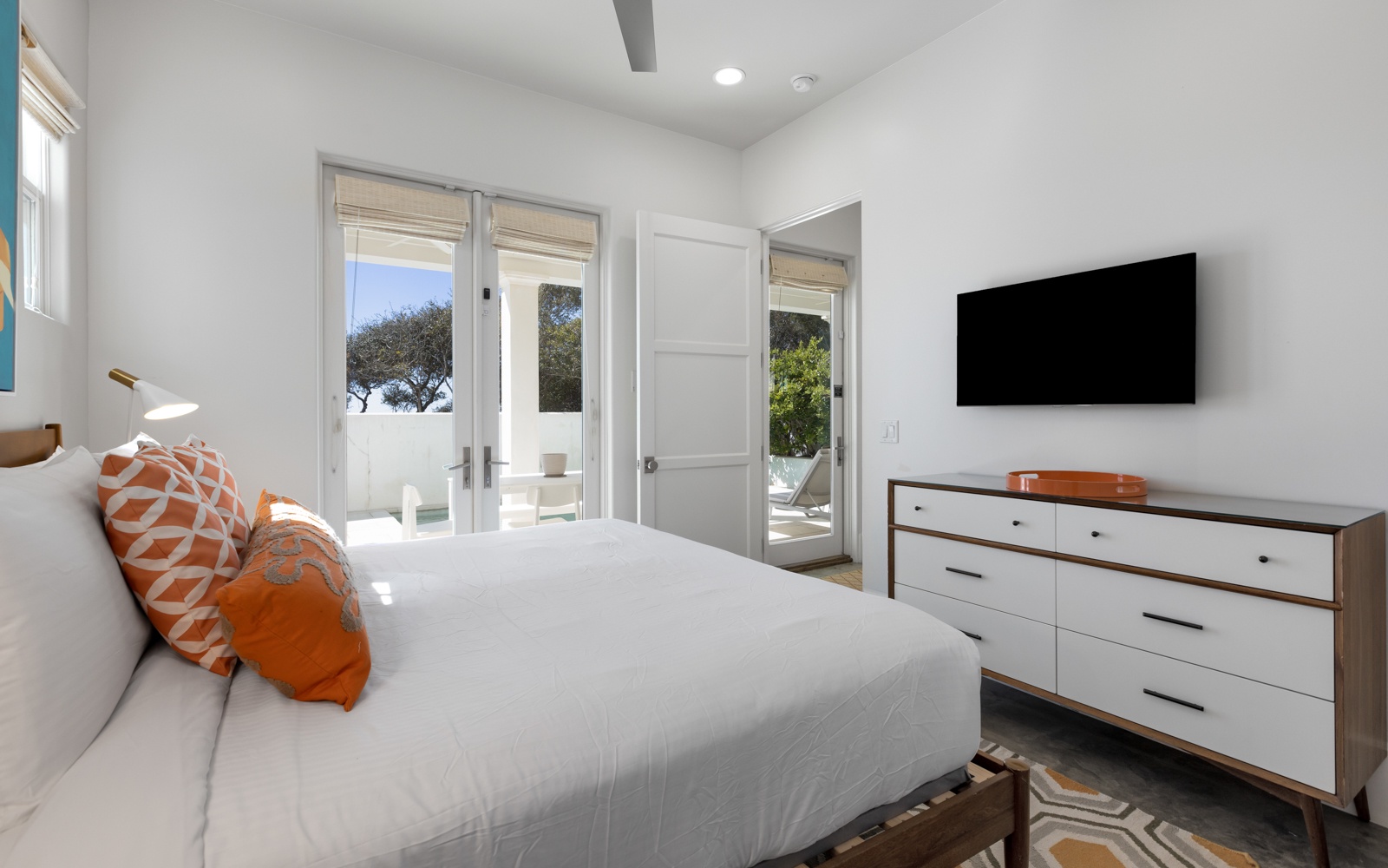 Relax in your bright bedroom with crisp white linens, vibrant orange accents, and French doors that open to your private outdoor retreat.