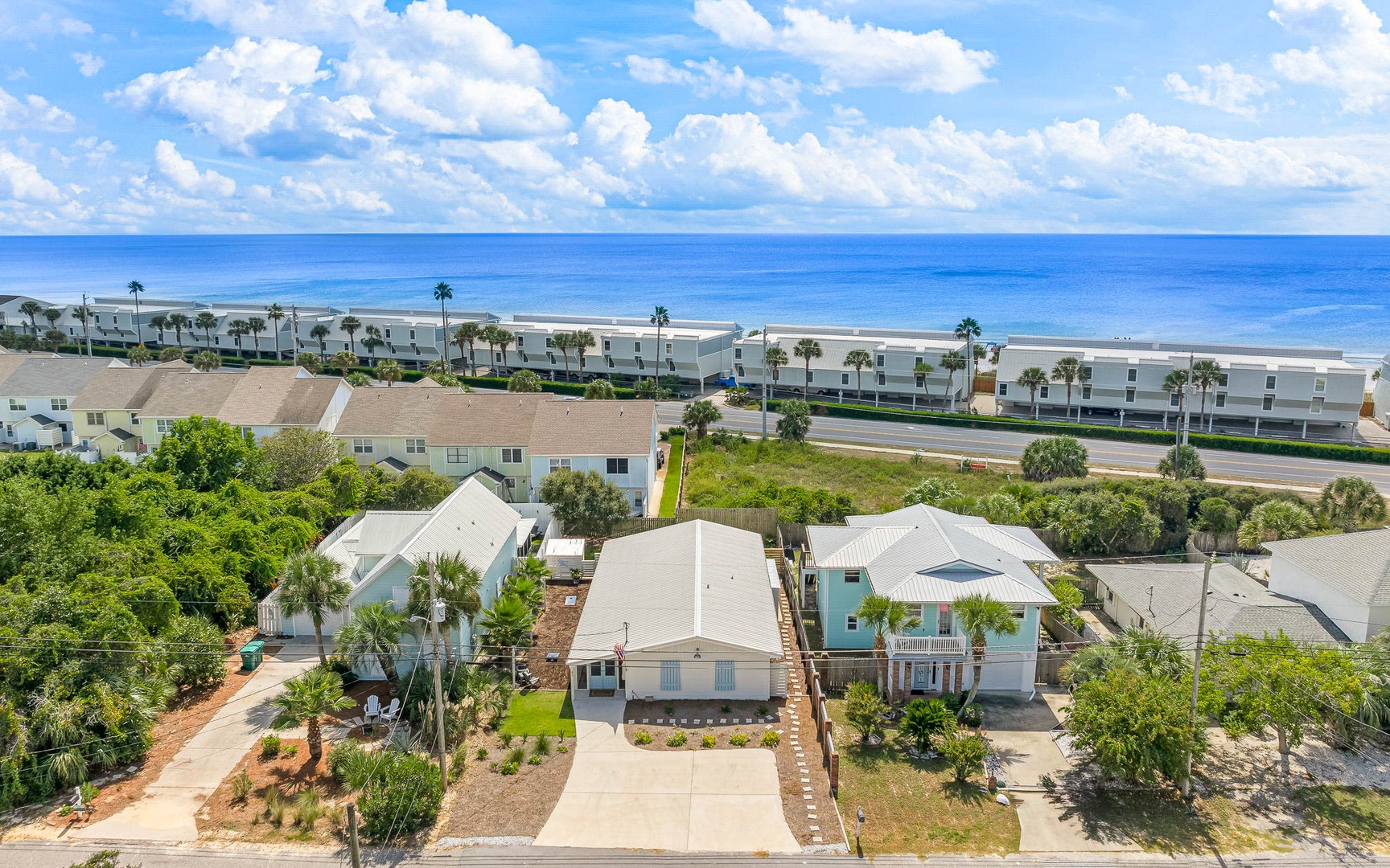 Aerial view showcases beachfront properties nestled among palm trees with pristine sandy beach and azure ocean stretching to the horizon.