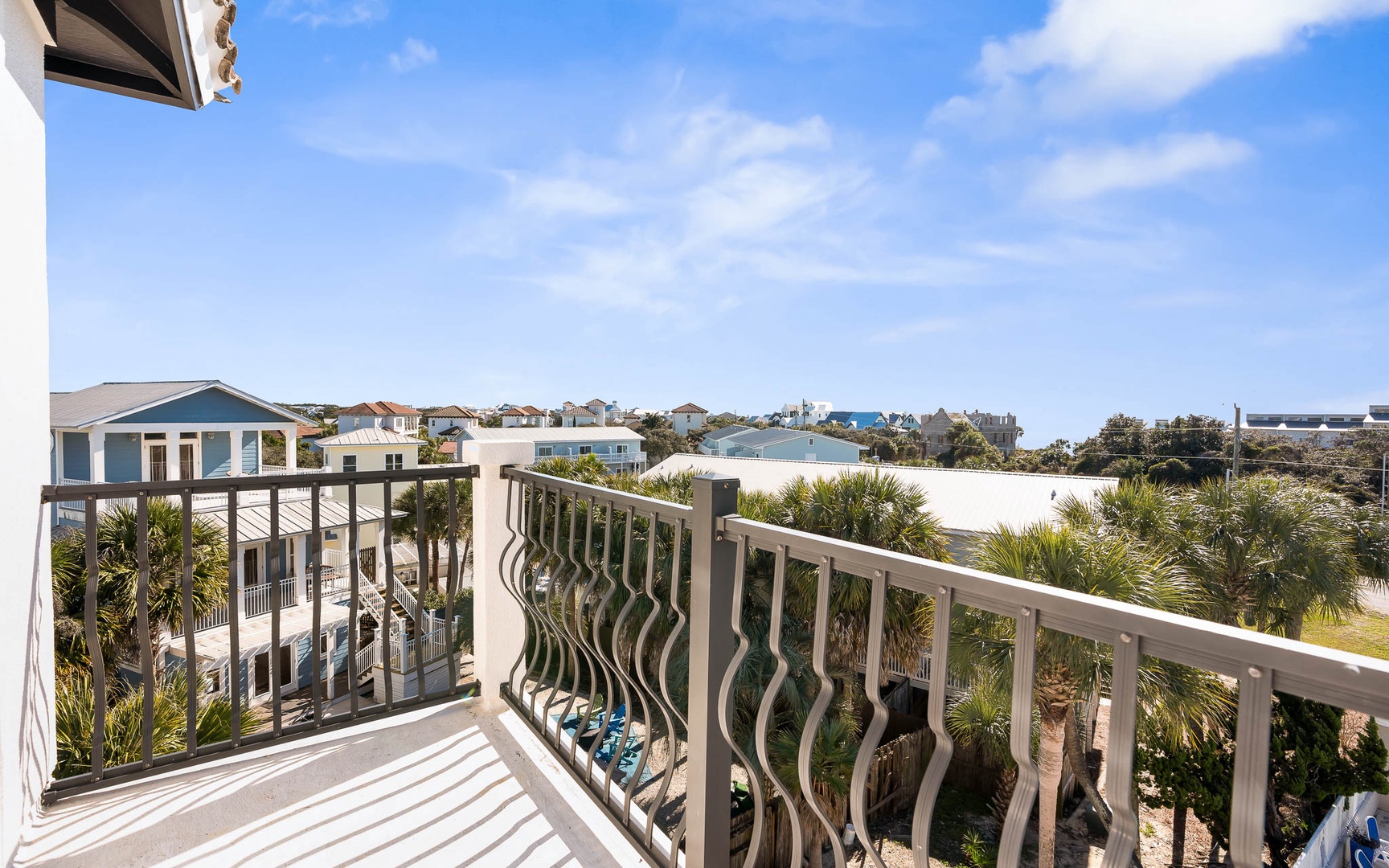 Private balcony with decorative railings overlooking coastal neighborhood homes and palm trees under bright blue skies.