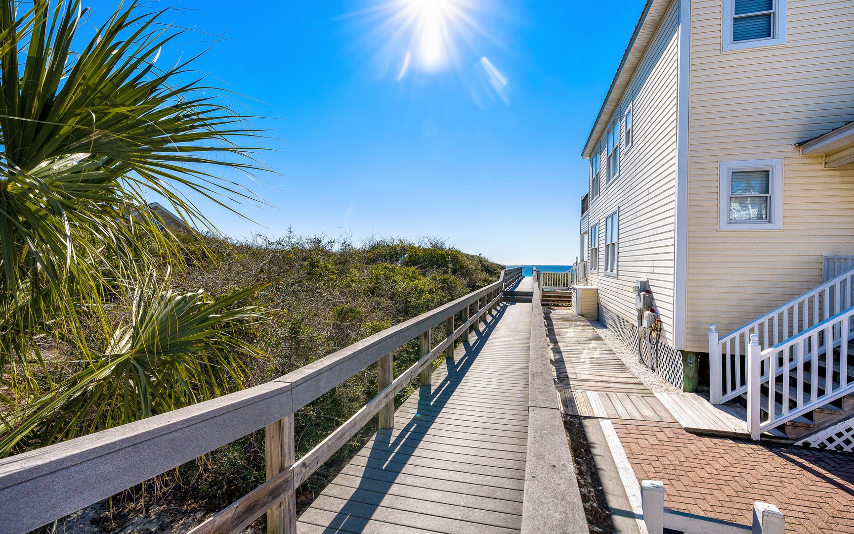 Beachfront property with private boardwalk leading through coastal dunes under brilliant sunshine.