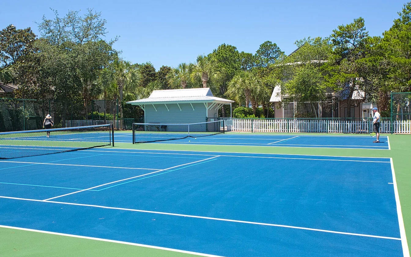 Professional tennis courts with pristine blue surfaces nestled among lush tropical landscaping and palm trees.