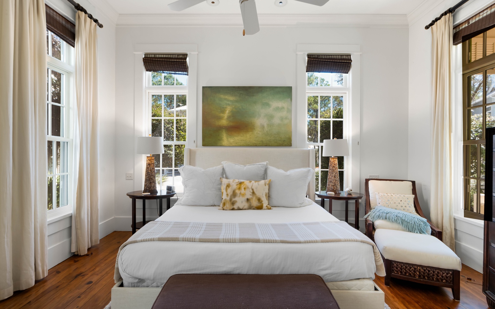 Your elegant bedroom features crisp white linens, warm hardwood floors, and natural light streaming through multiple windows for peaceful mornings.