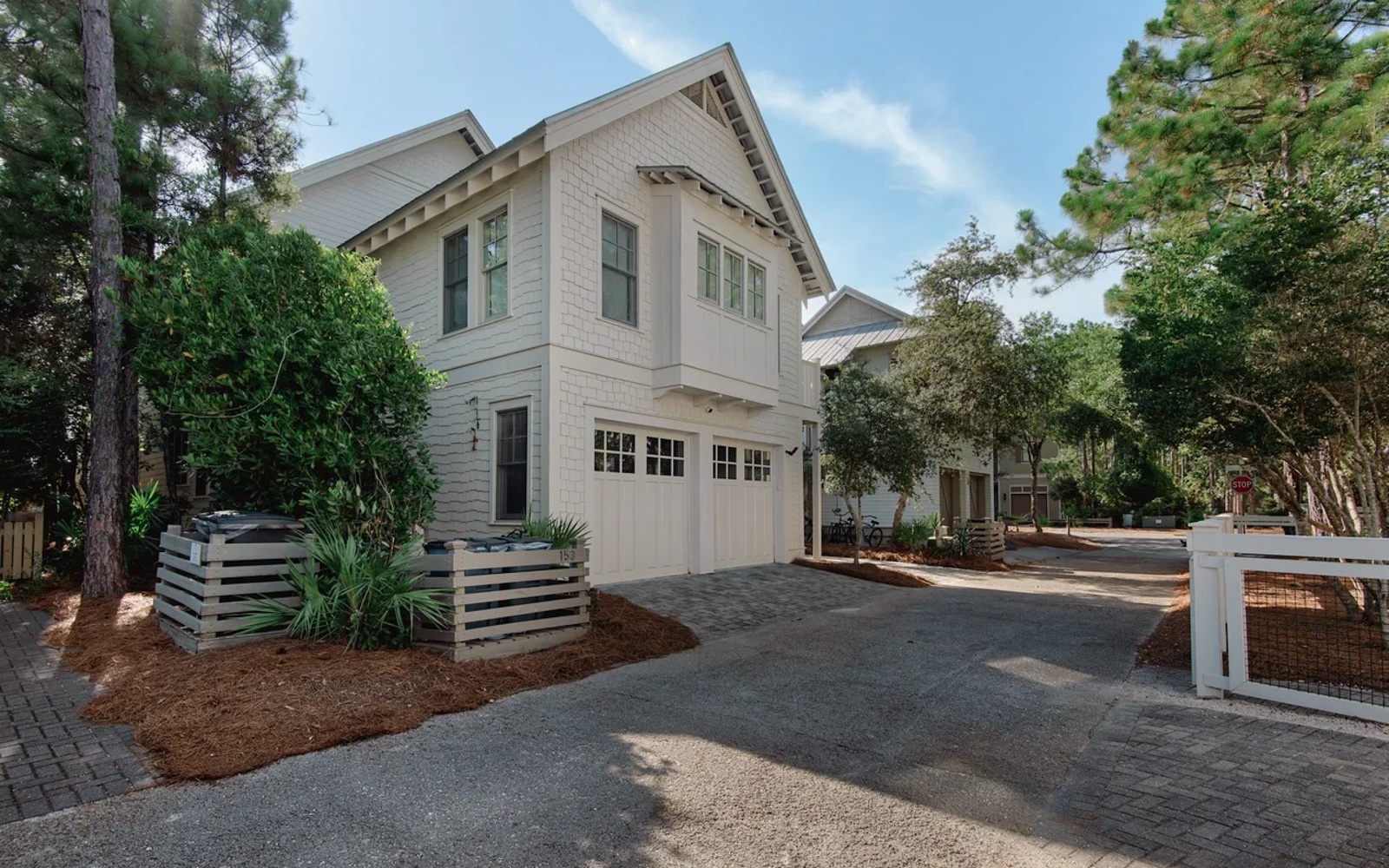 Charming coastal cottage with pristine white siding and welcoming entrance, nestled among lush mature trees in a peaceful neighborhood setting.