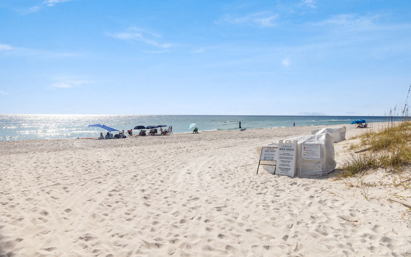 Sandy beach stretches along sparkling waters with beach umbrellas and visitors enjoying the coastal setting.