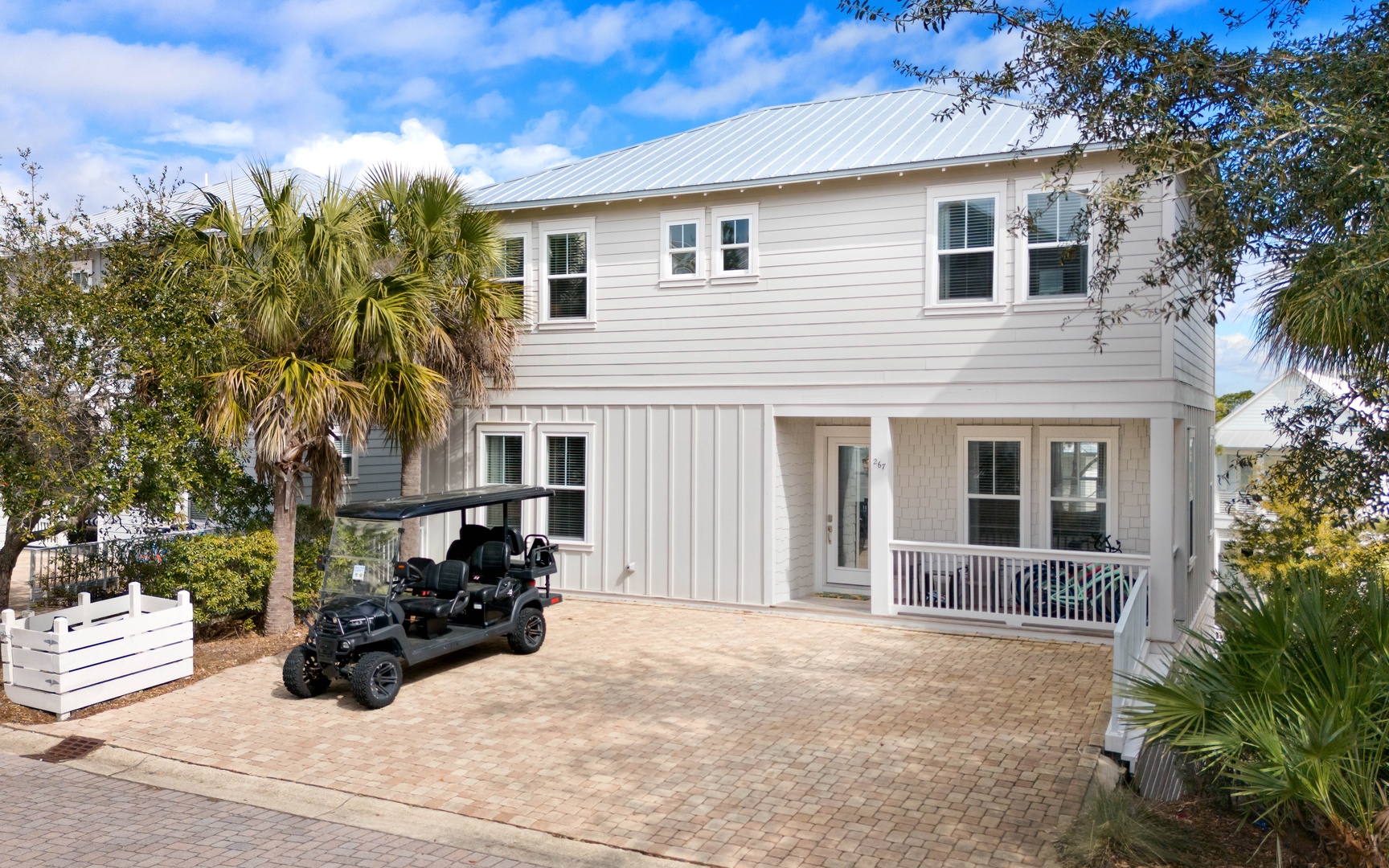 Contemporary two-story beach house with covered parking and tropical landscaping in a coastal neighborhood setting.