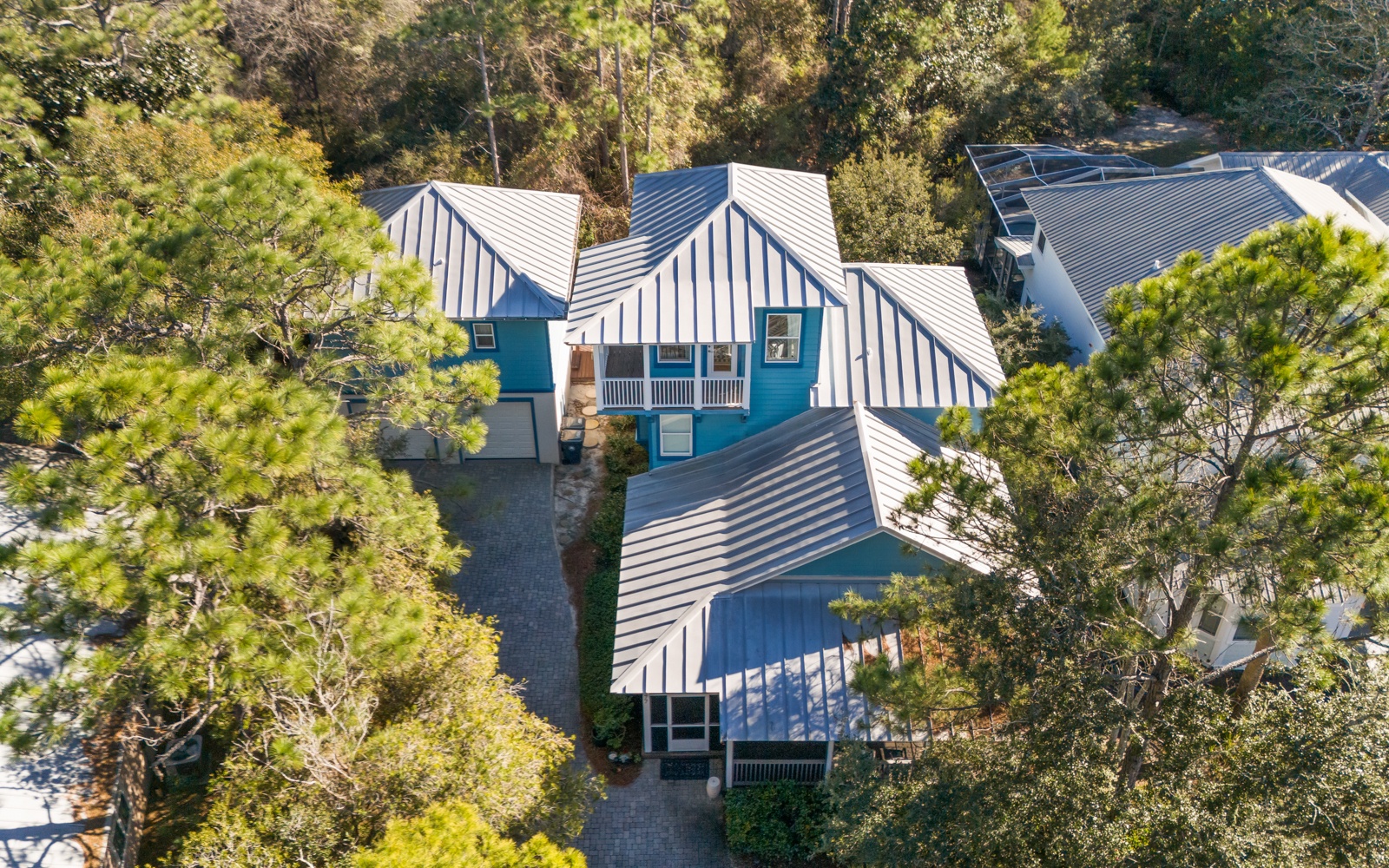 Charming blue cottage nestled among mature trees with distinctive metal roofing and private outdoor spaces in a peaceful residential setting.