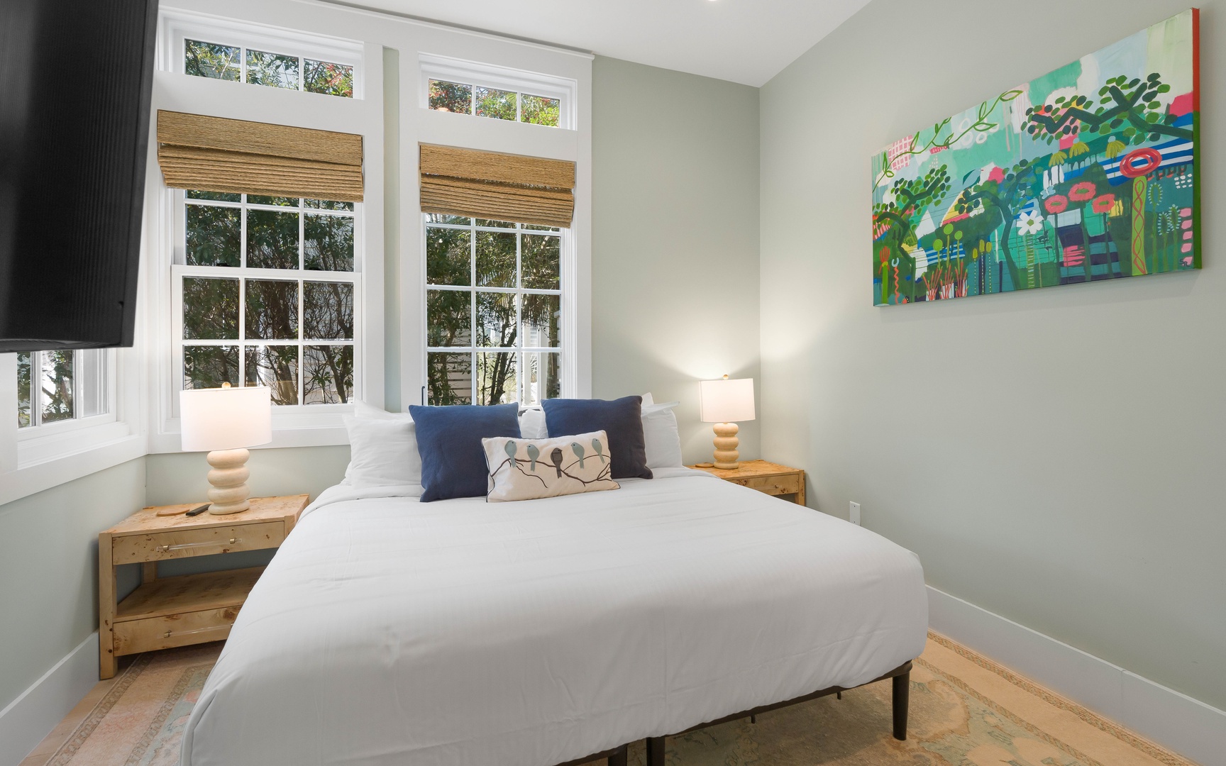 Drift into peaceful dreams in your serene bedroom, where soft morning light filters through bamboo blinds and colorful artwork brightens the walls.