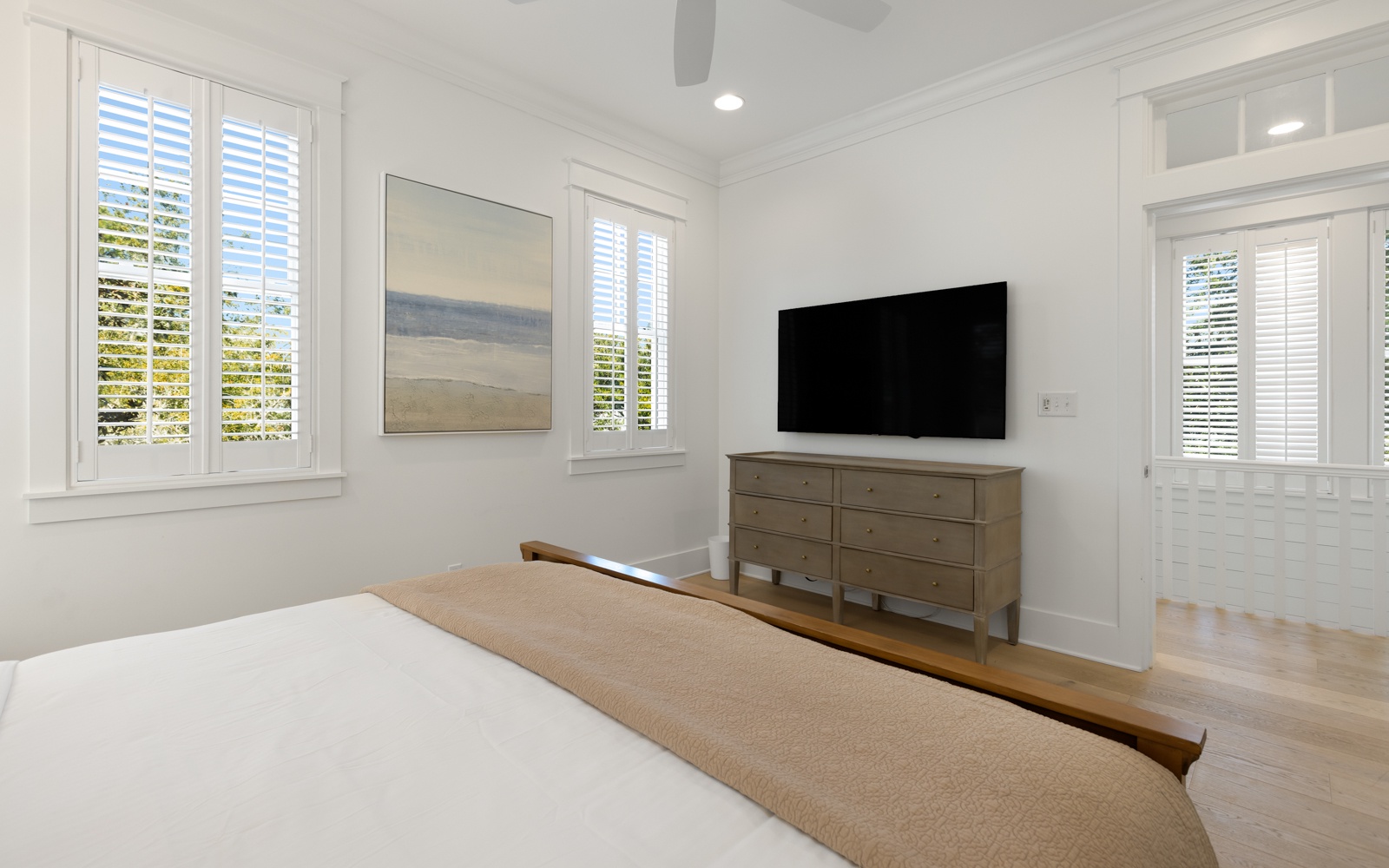 Relax in your bright, serene bedroom with crisp white linens, modern amenities, and peaceful garden views through plantation shutters.