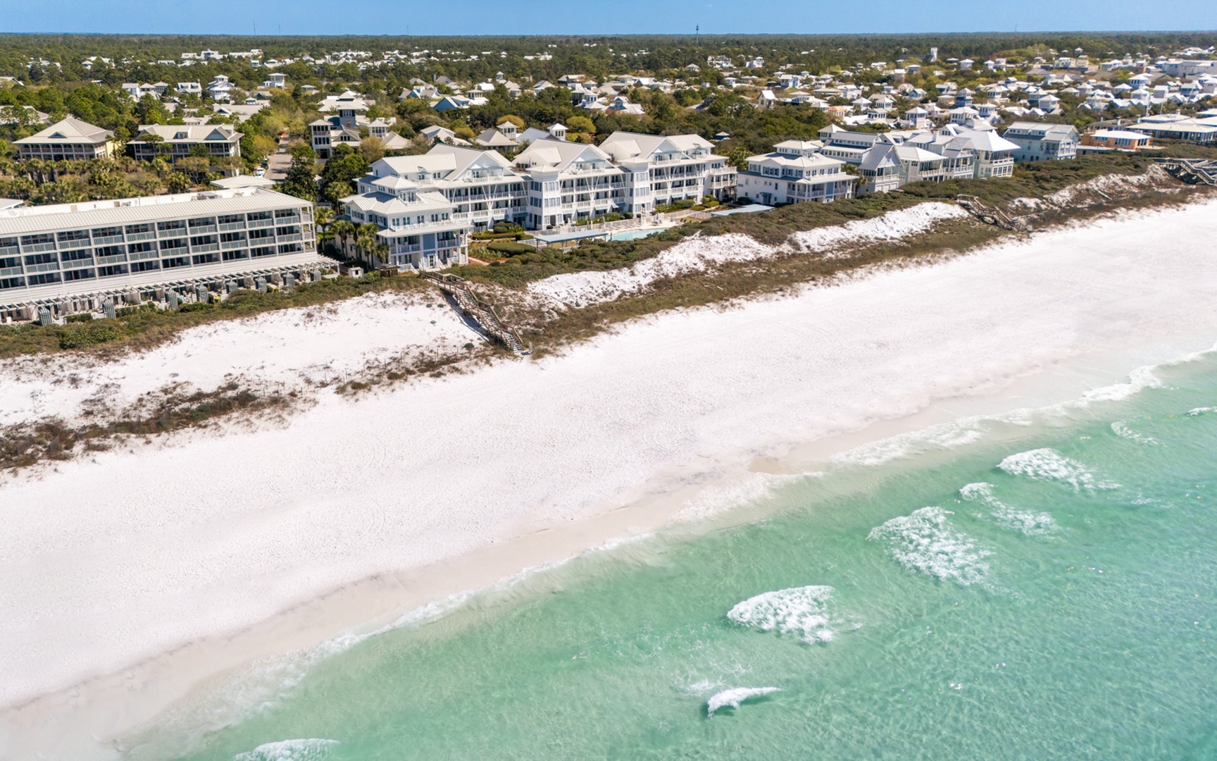 Stunning aerial view of beachfront properties along pristine white sand and turquoise waters in a peaceful coastal community.