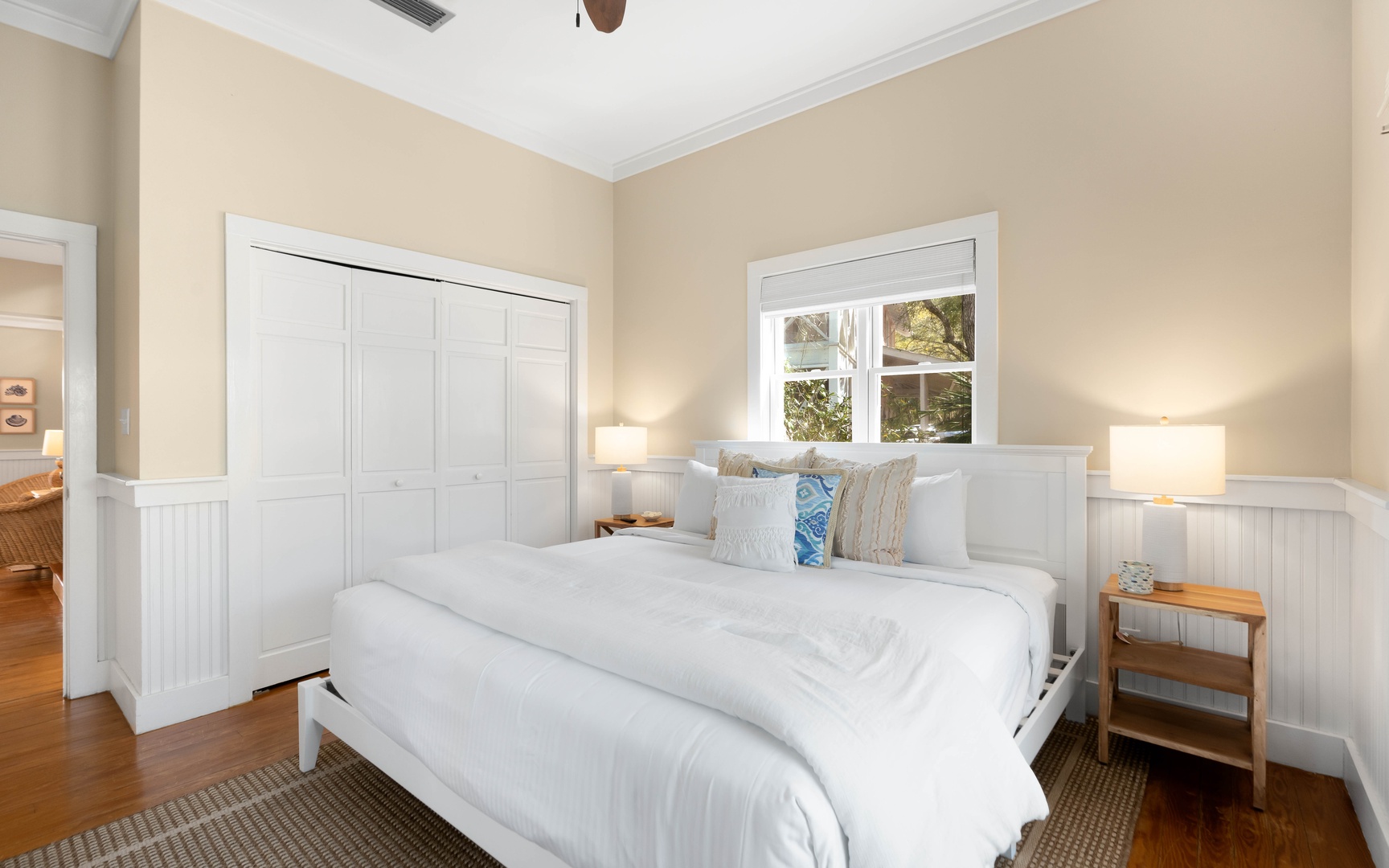 Sink into plush white linens in your peaceful retreat, where warm beige walls and crisp white wainscoting create a cozy sanctuary for restful nights.