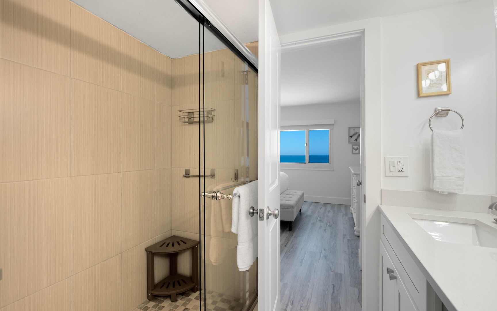 Your private spa-like bathroom features a spacious glass shower and pristine marble vanity, with glimpses of the sea view bedroom beyond.
