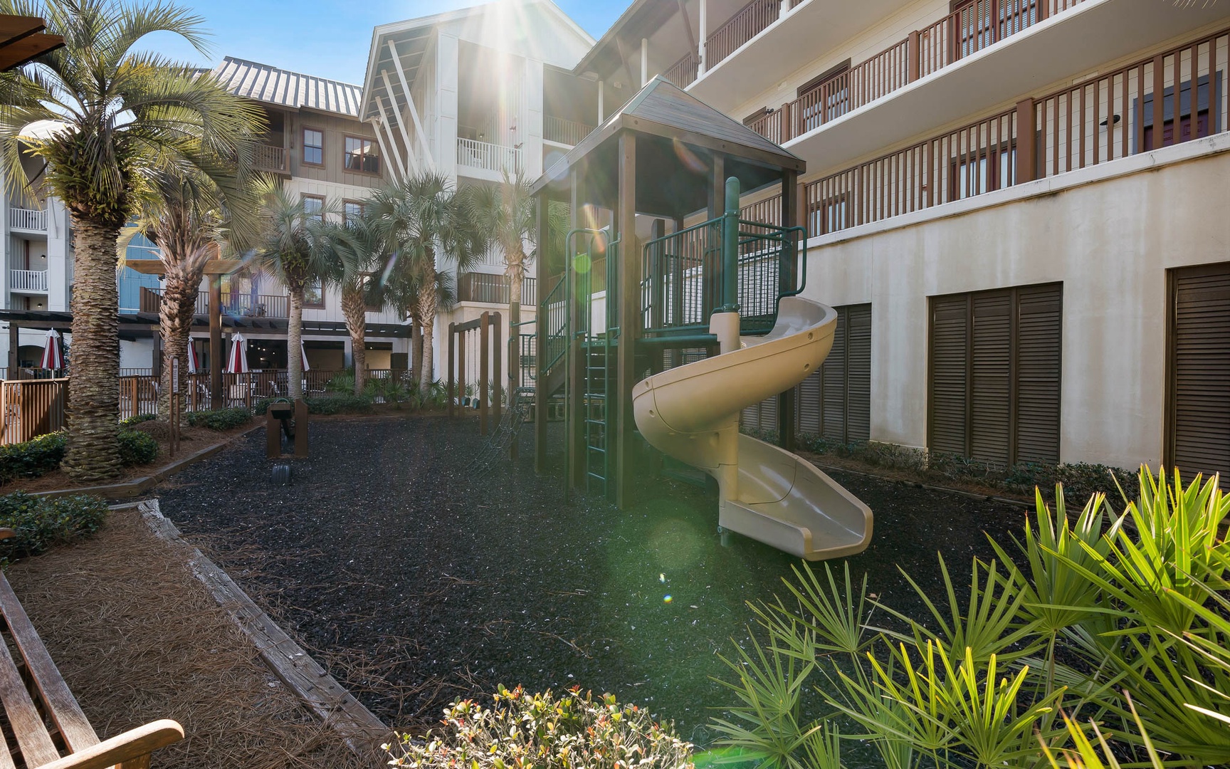 The property features an exciting water slide descending into a refreshing pool, surrounded by tropical palm trees and multi-level accommodations.