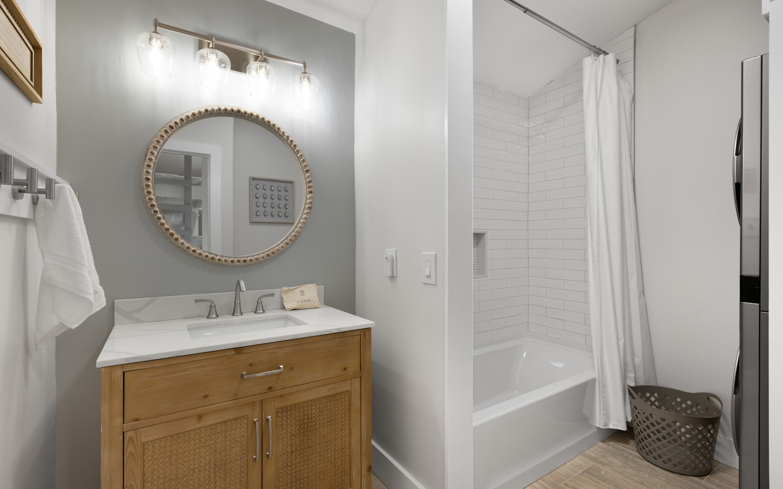 Step into your stylish bathroom featuring a warm wood vanity, elegant round mirror, and refreshing tub-shower combo for unwinding after adventures.