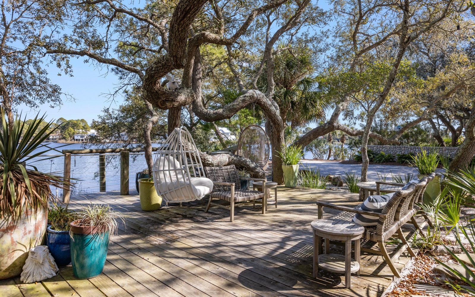 Unwind in your private waterfront oasis with hanging chairs and loungers beneath towering trees, overlooking tranquil waters.