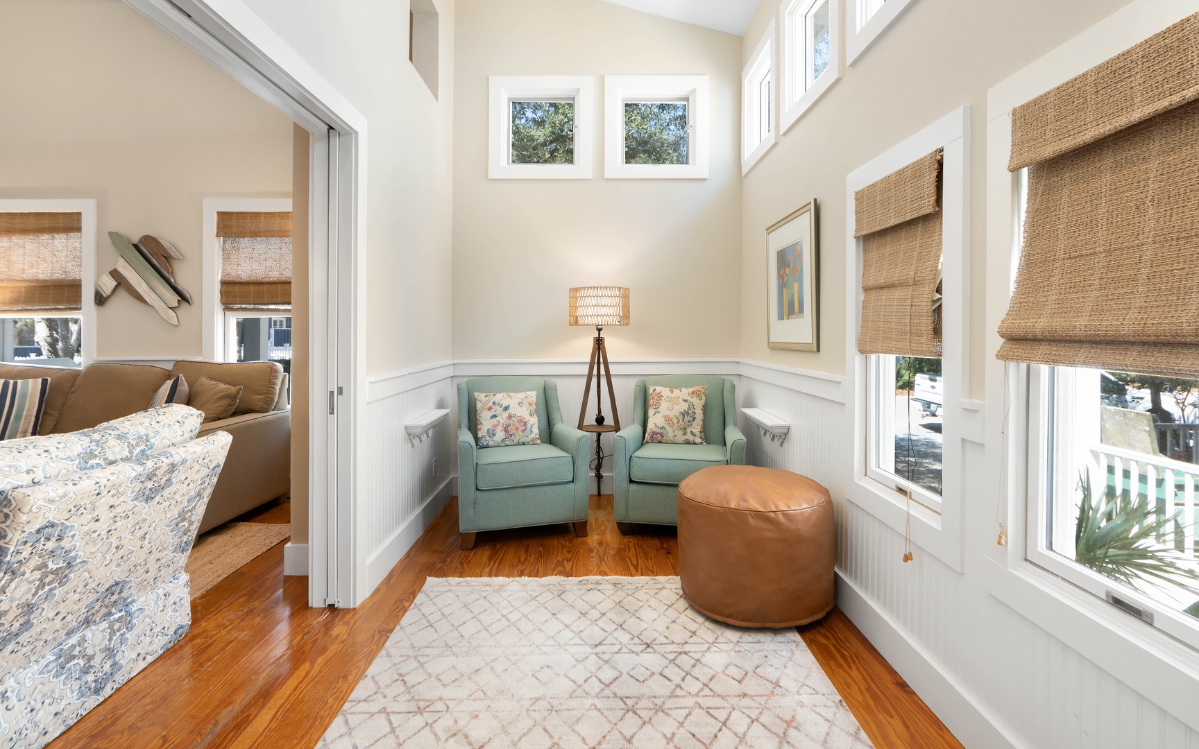 Your peaceful reading nook awaits with twin seafoam chairs, warm leather ottoman, and natural light streaming through bamboo shades.
