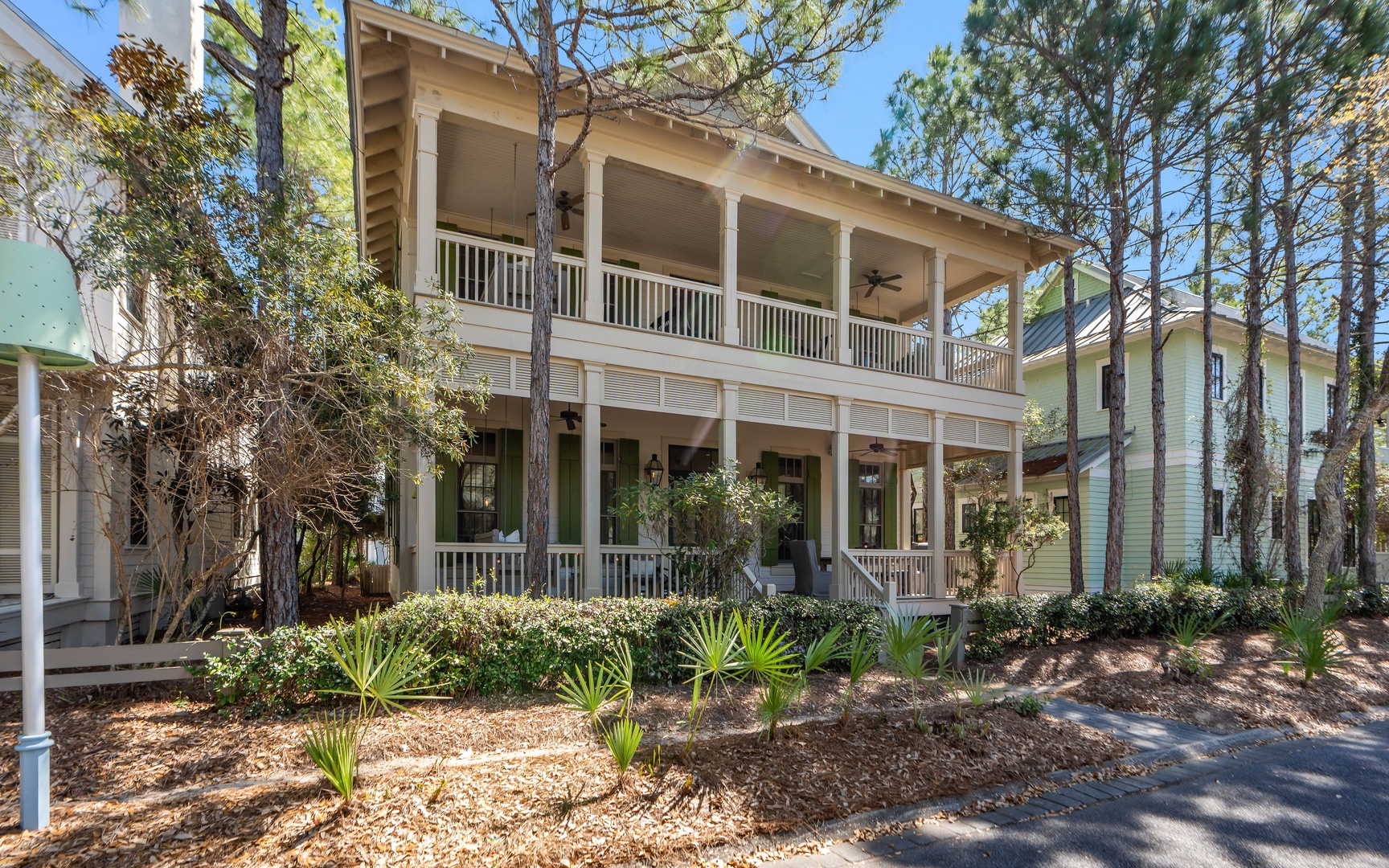 Charming coastal home with wraparound porches nestled among towering pines and native landscaping in a peaceful neighborhood setting.
