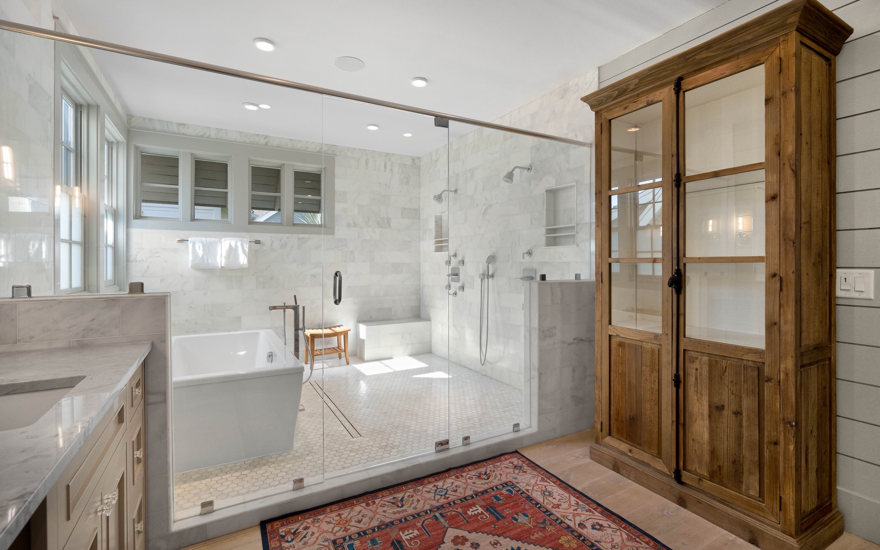 Your spa-like bathroom features a luxurious soaking tub and spacious walk-in shower with marble accents and rustic wood storage.