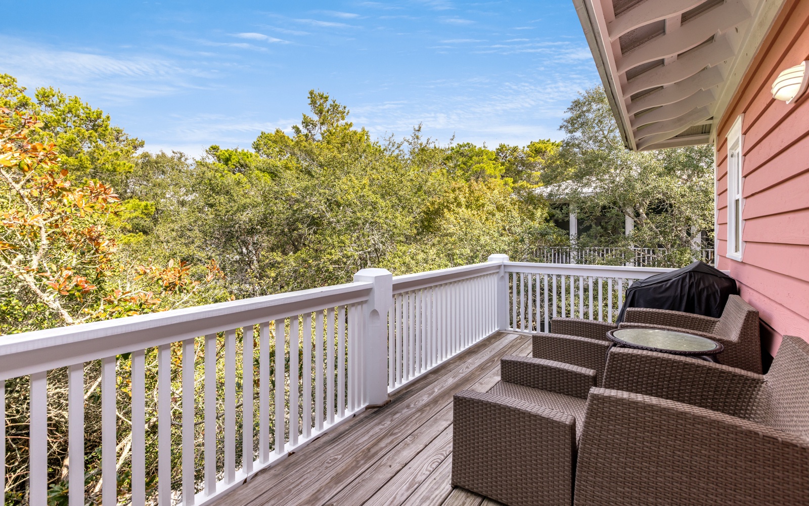 Relax in comfortable wicker seating on your private deck, surrounded by lush trees and peaceful blue skies.