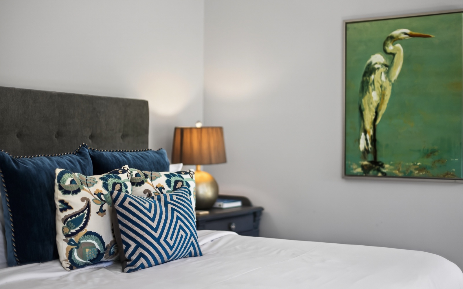 Sink into plush pillows and crisp linens in your serene retreat, where coastal artwork and warm lighting create the perfect atmosphere for restful nights.