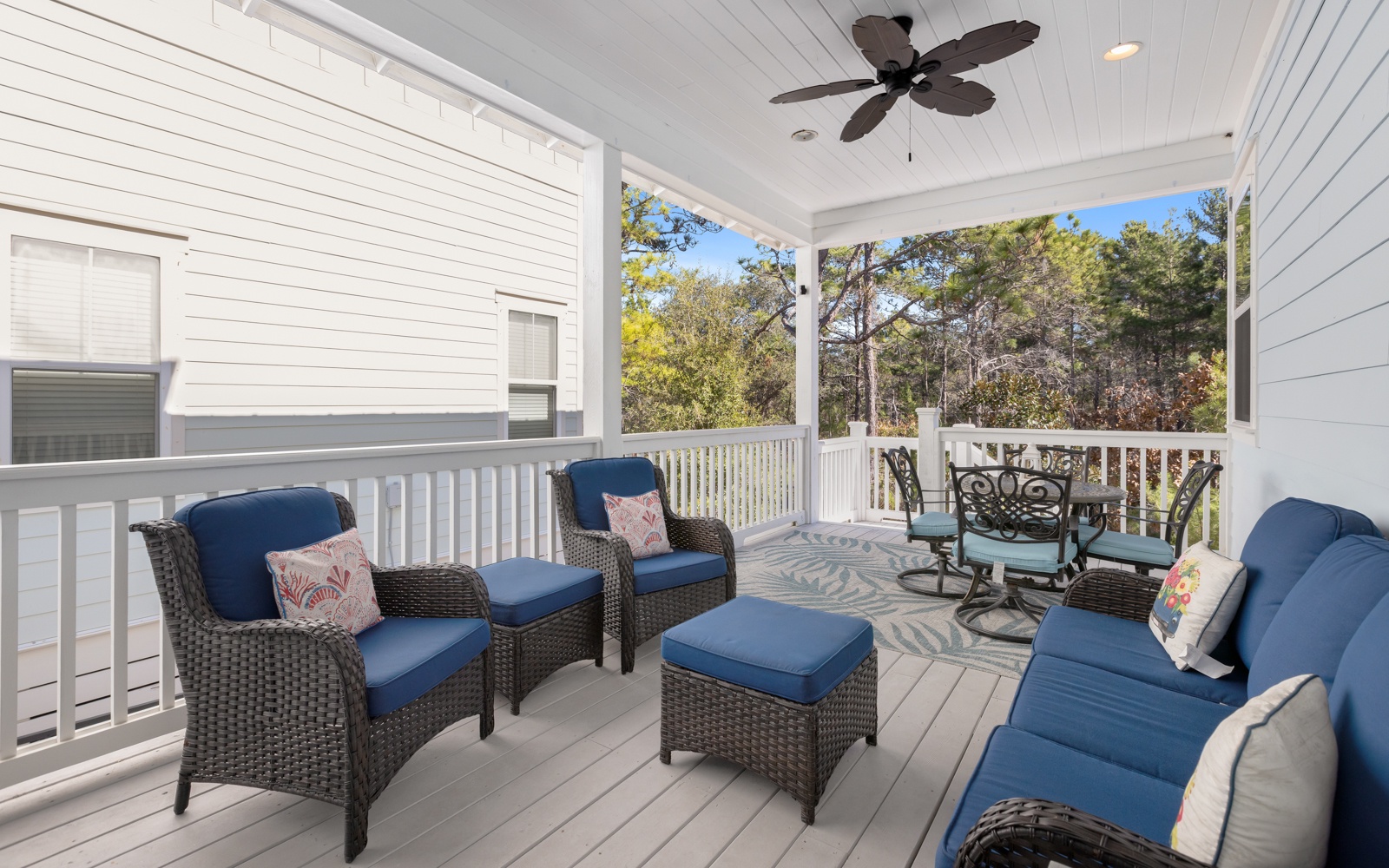 Unwind on your private covered porch with comfortable seating and ceiling fan, overlooking peaceful wooded surroundings.