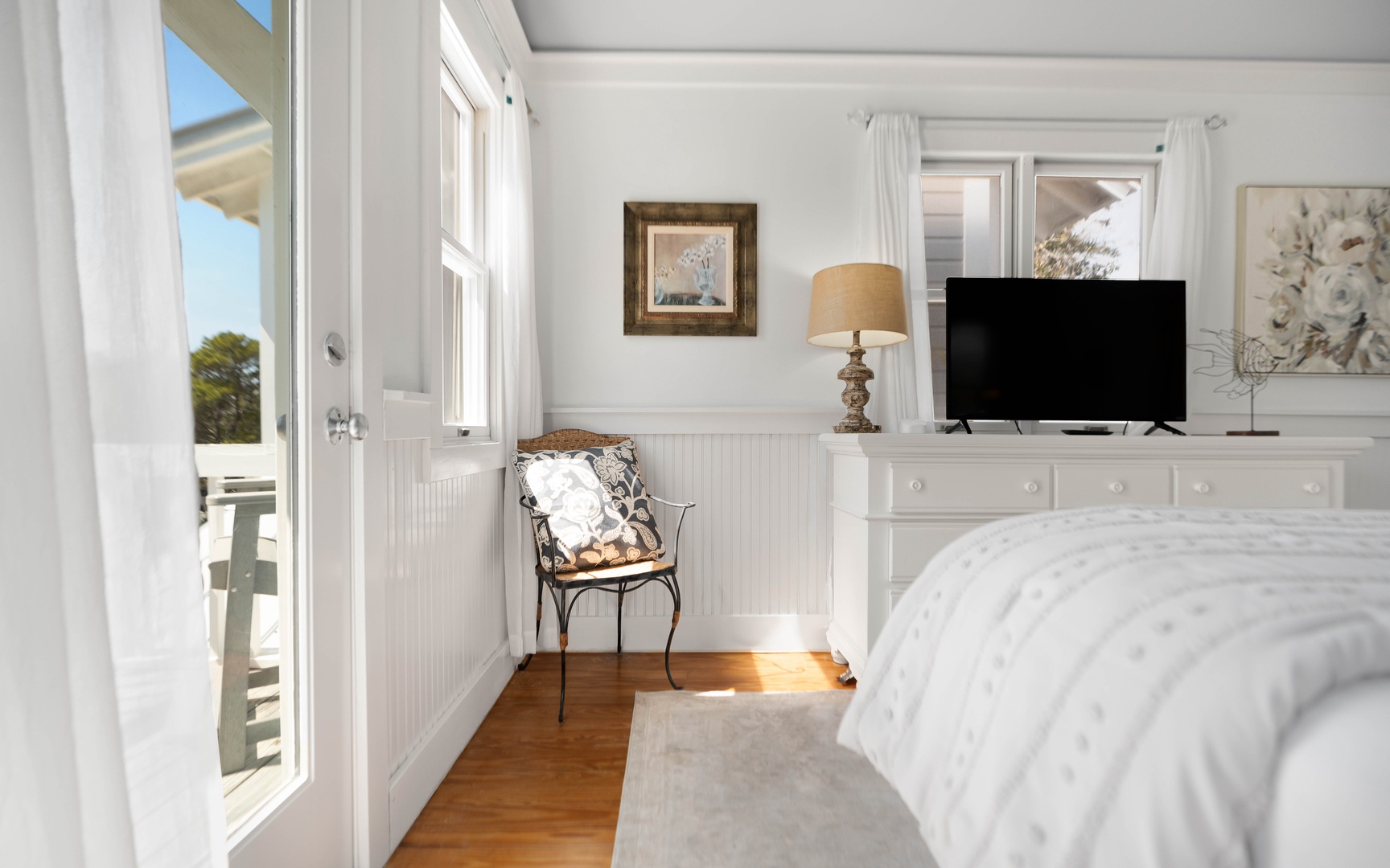 Wake up to soft morning light streaming through your windows in this charming coastal bedroom with crisp white linens and TV.