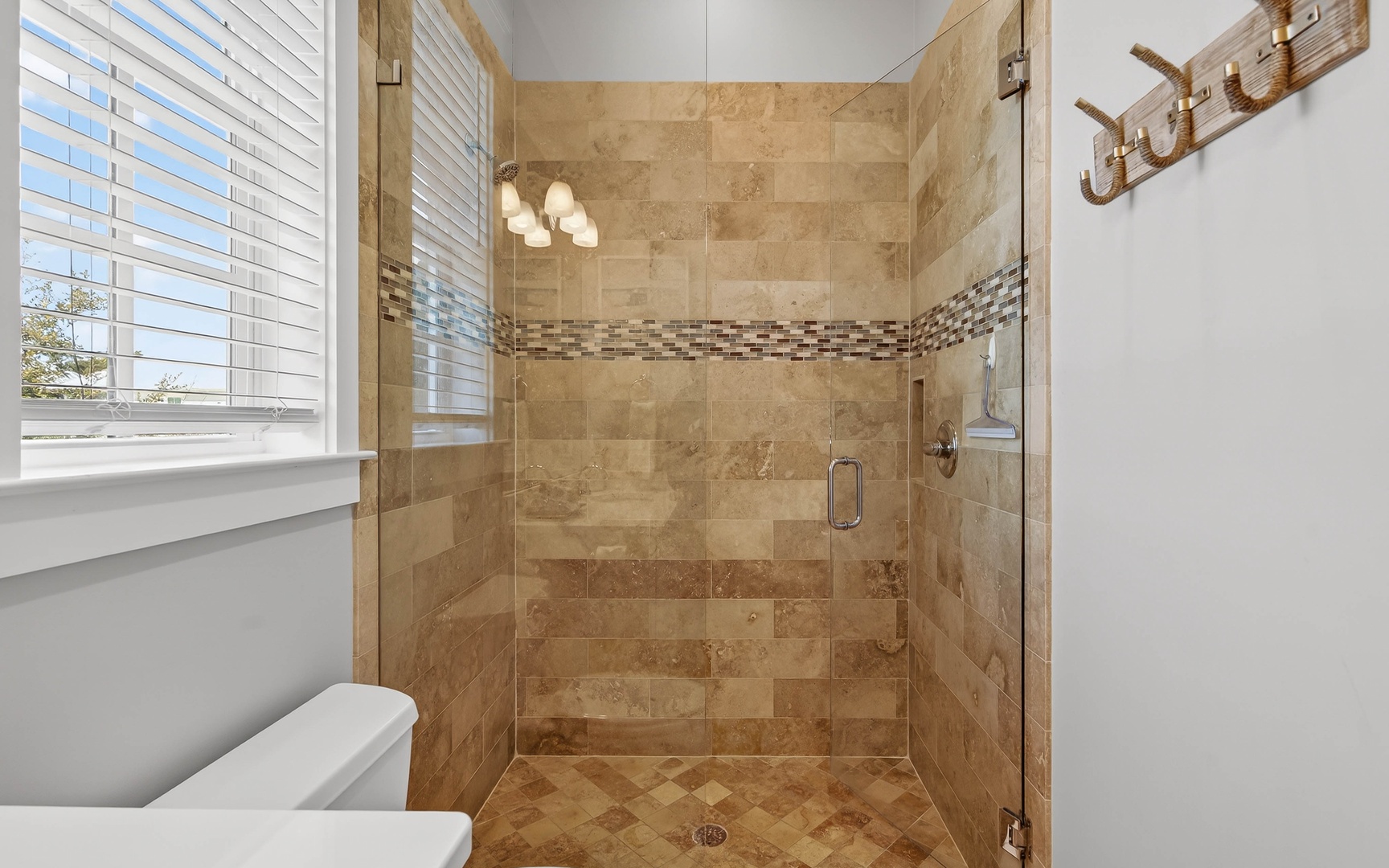 Step into your luxurious tiled shower with beautiful mosaic accents and glass doors, where warm natural light creates the perfect morning retreat.