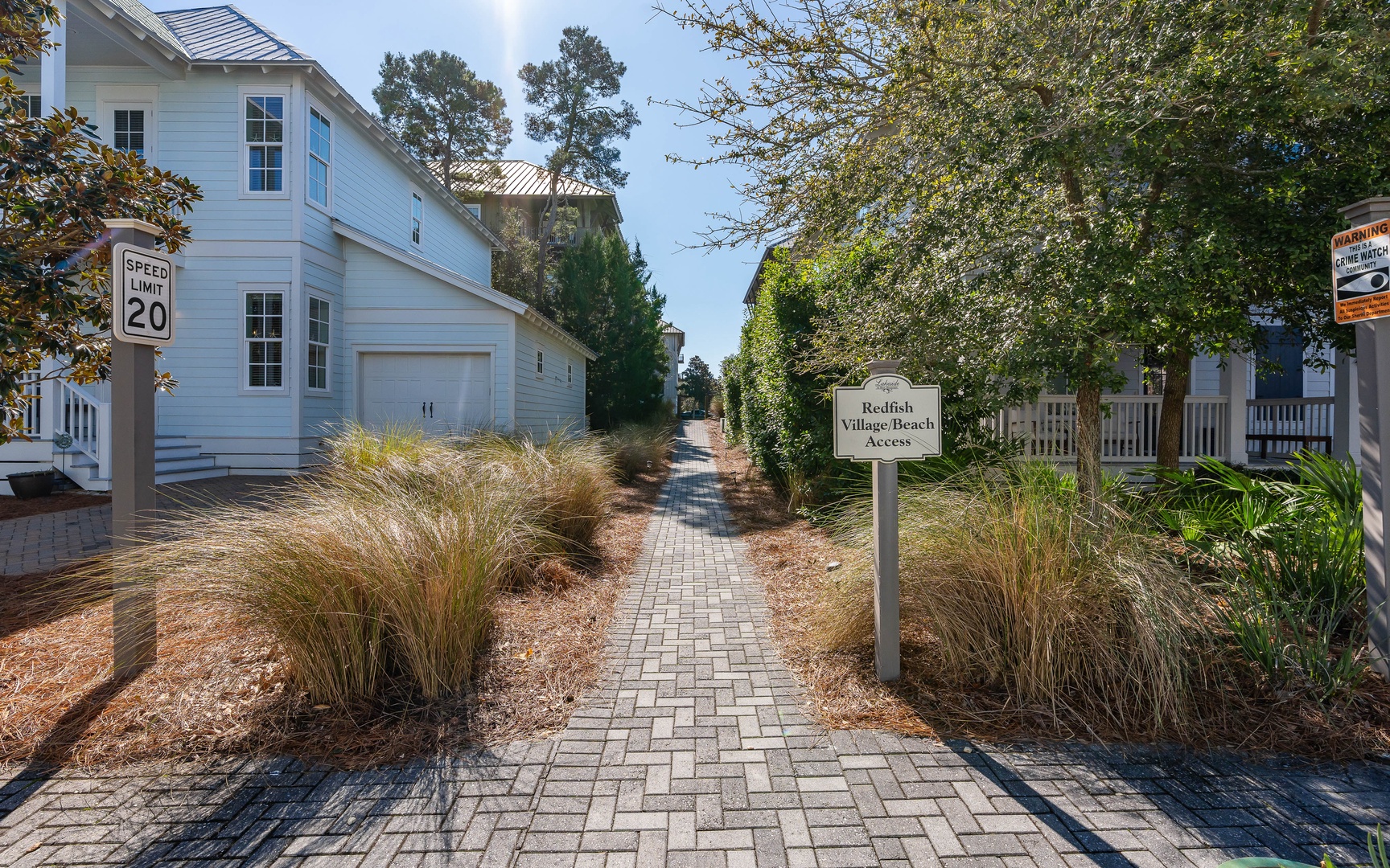 Charming coastal community entrance with brick pathways leading to elegant beach homes surrounded by native landscaping.