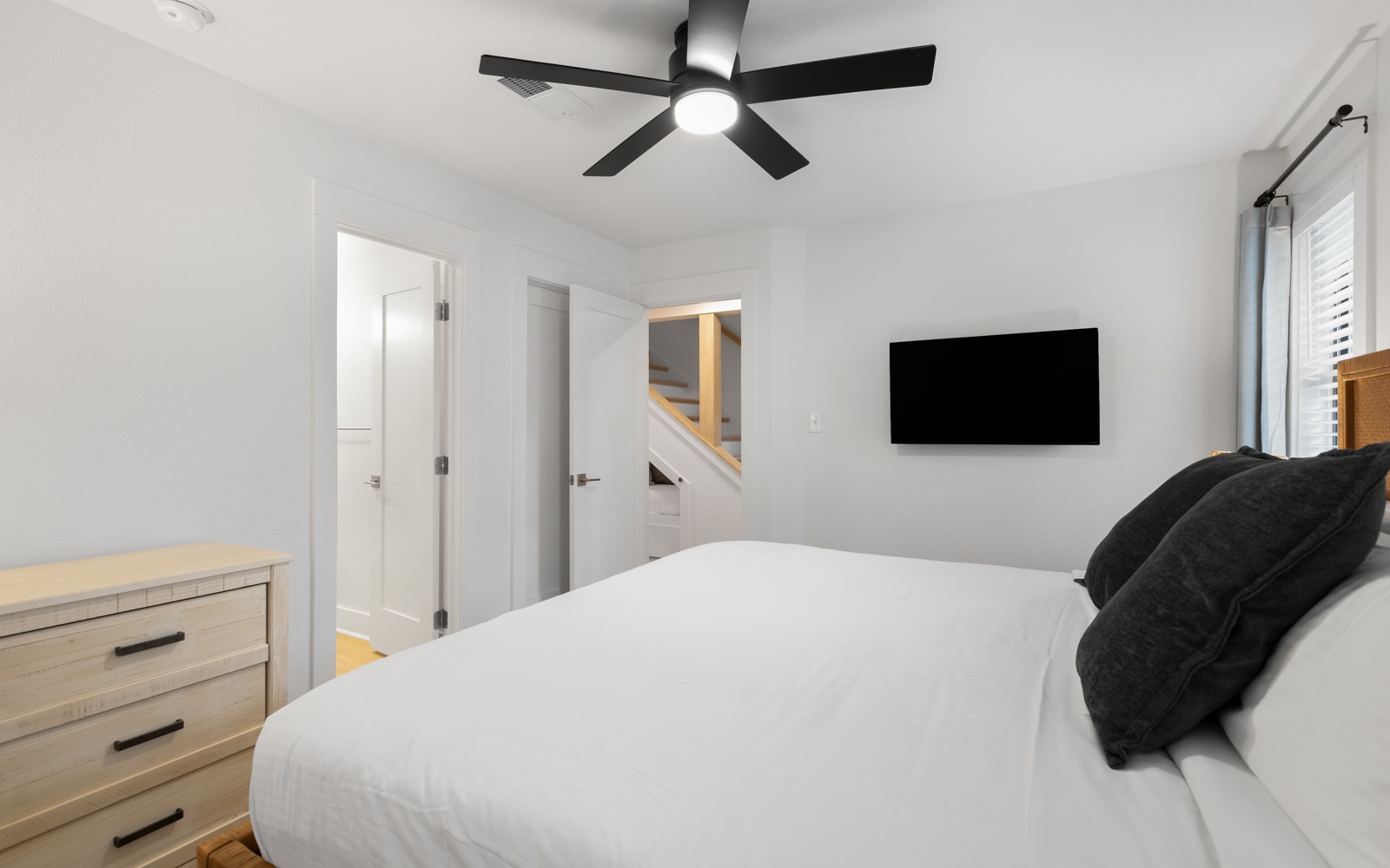 Drift off in your serene bedroom with crisp linens, modern ceiling fan, and wall-mounted TV for relaxation.