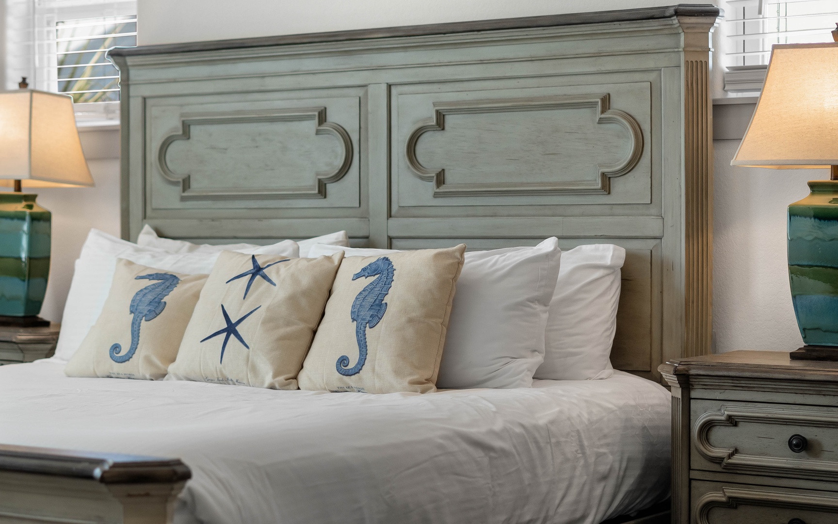 Drift into coastal dreams on crisp white linens, surrounded by charming seahorse pillows and weathered wood furniture that whispers of ocean breezes.