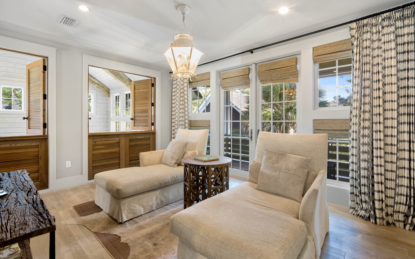 Sink into plush armchairs in your elegant sitting area, where coastal charm meets comfort with bamboo blinds and French doors opening to your private balcony.
