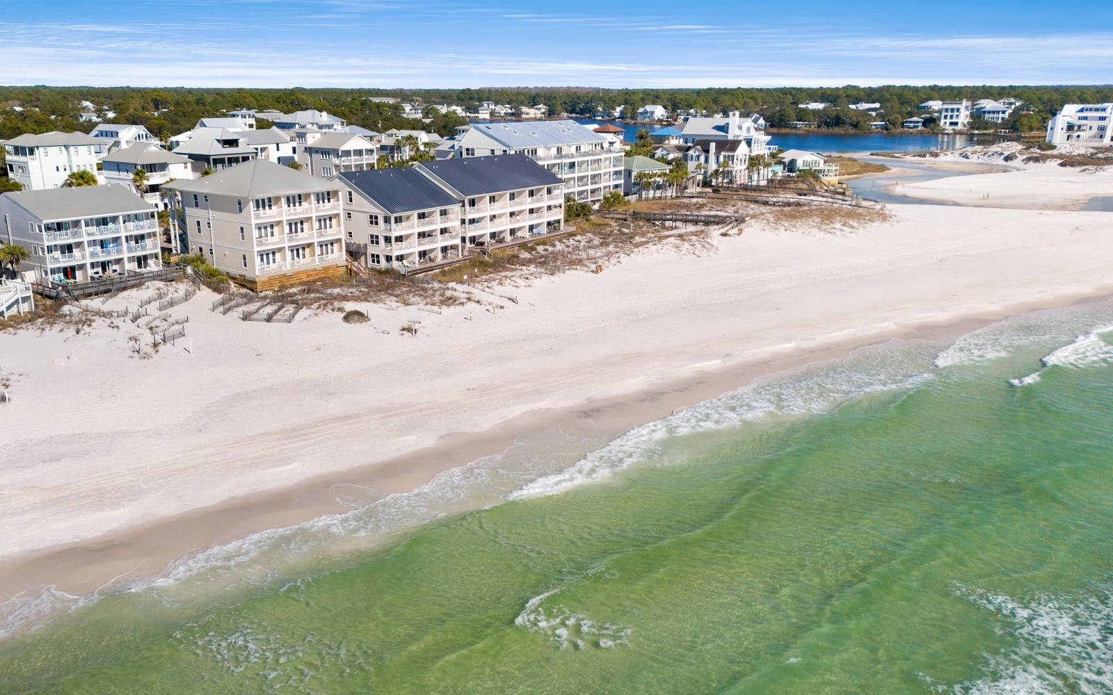 Stunning aerial view of beachfront properties along pristine white sand beach with emerald Gulf waters.