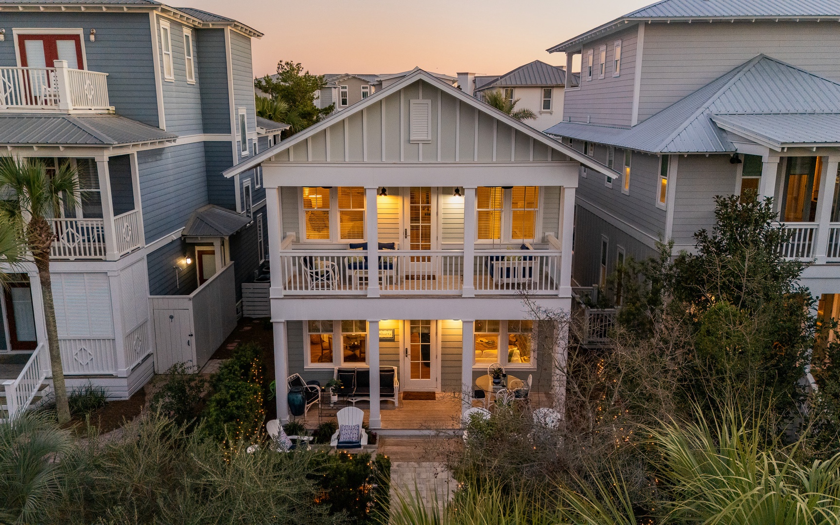 Coastal beach house nestled in charming neighborhood at golden hour, featuring classic architecture and warm interior lighting.