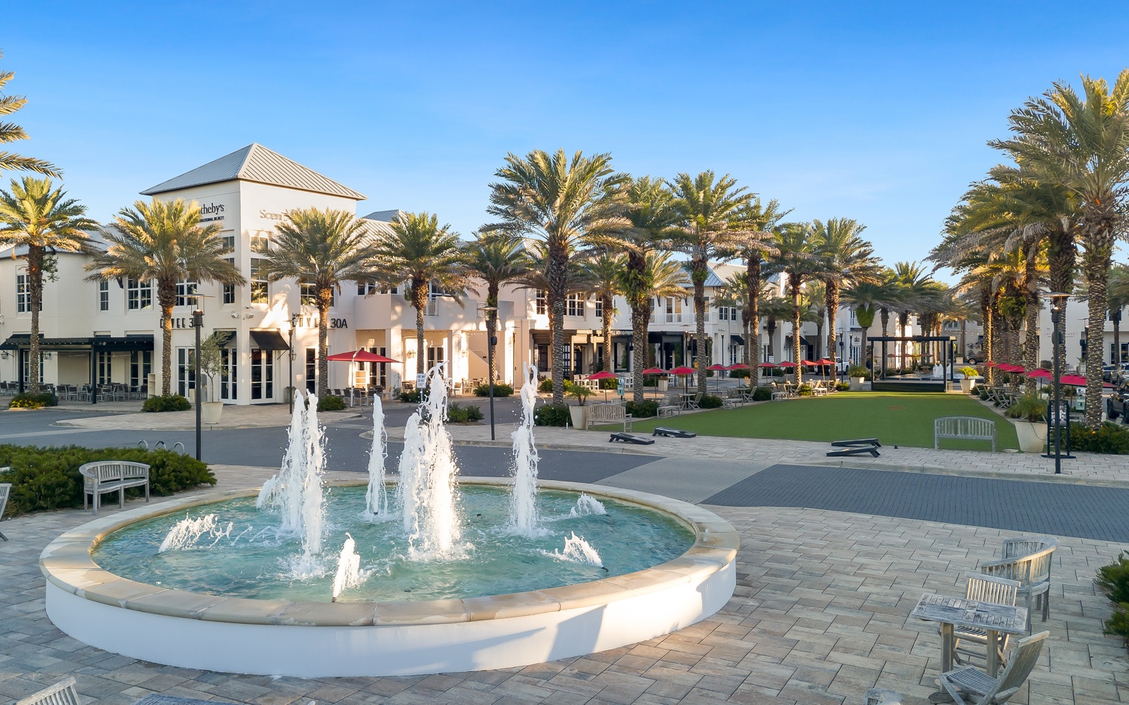 A charming town center with palm-lined shops and peaceful fountain, creating an inviting atmosphere for leisurely strolls and exploration.