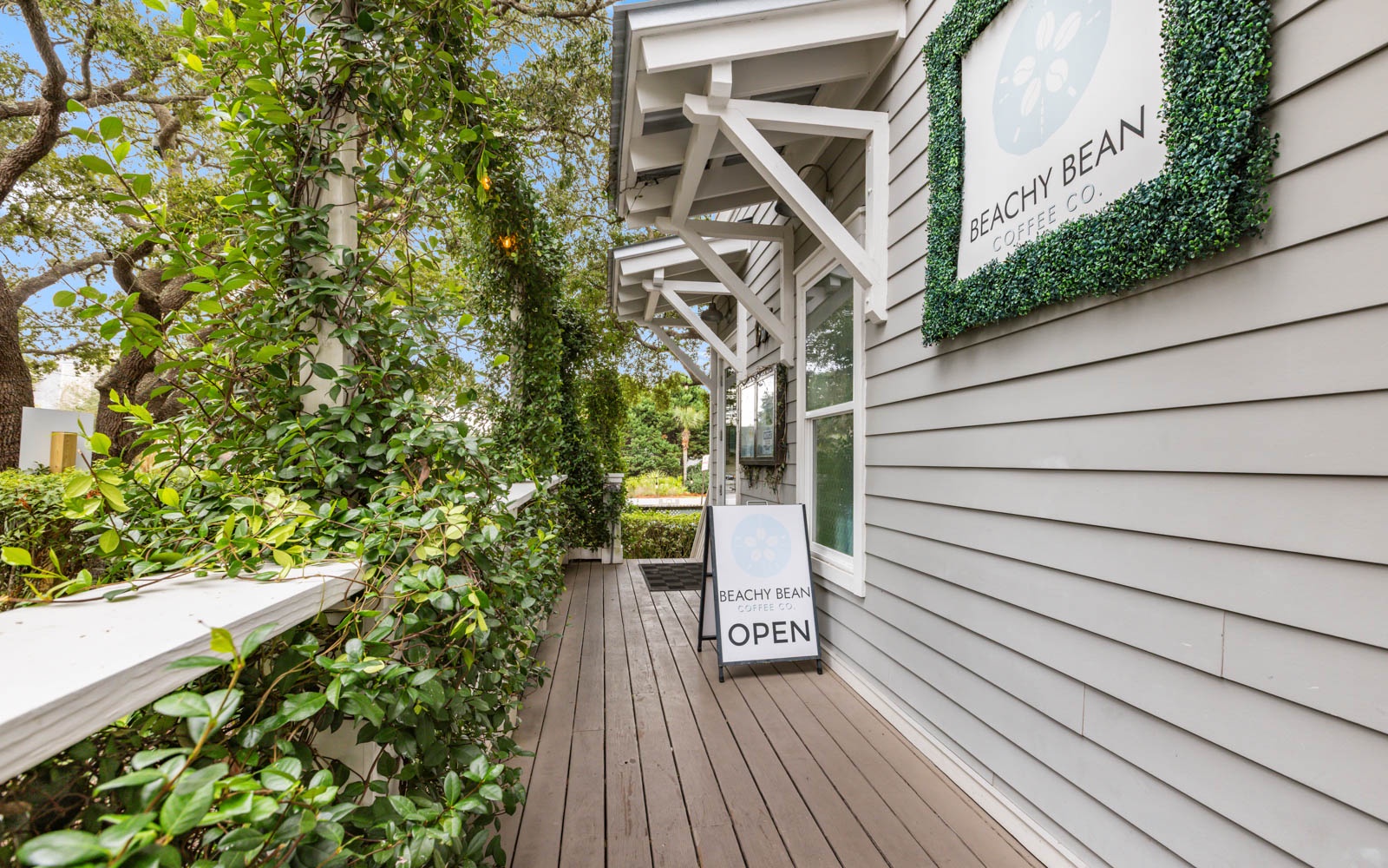 Beachy Bean cafe entrance with lush greenery and welcoming outdoor deck creates a charming coastal dining destination.