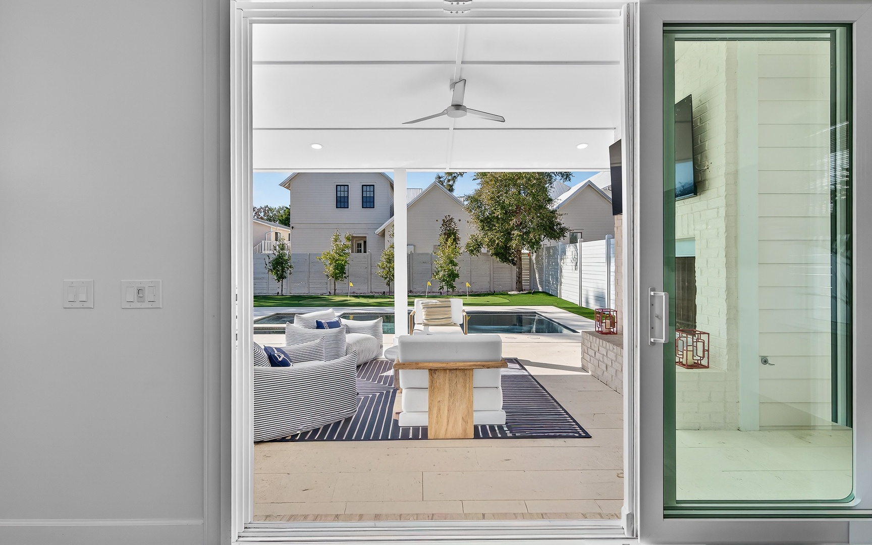 Your modern patio flows seamlessly outdoors through glass doors, revealing designer seating and a sparkling pool beyond.