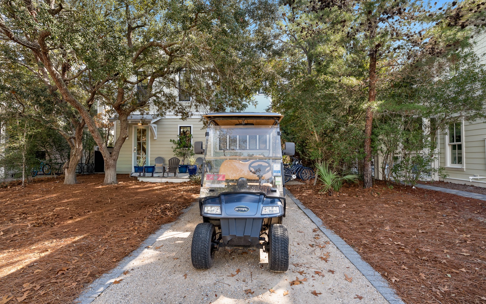 A charming property entrance features mature oak trees and a welcoming driveway, with a convenient golf cart for easy neighborhood exploration.