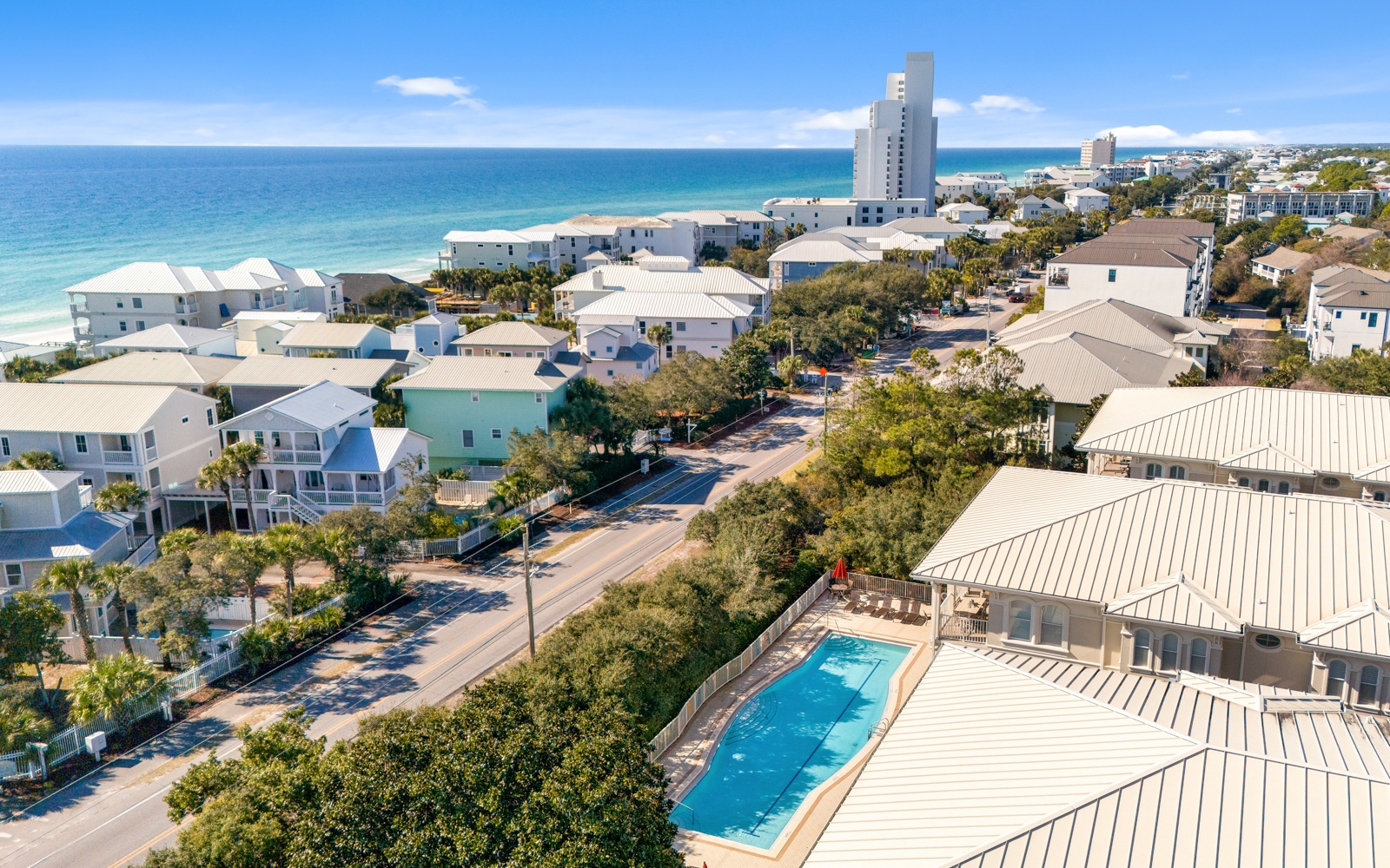 Aerial view of beachfront vacation rental community with swimming pool, coastal homes, and pristine turquoise waters nearby.
