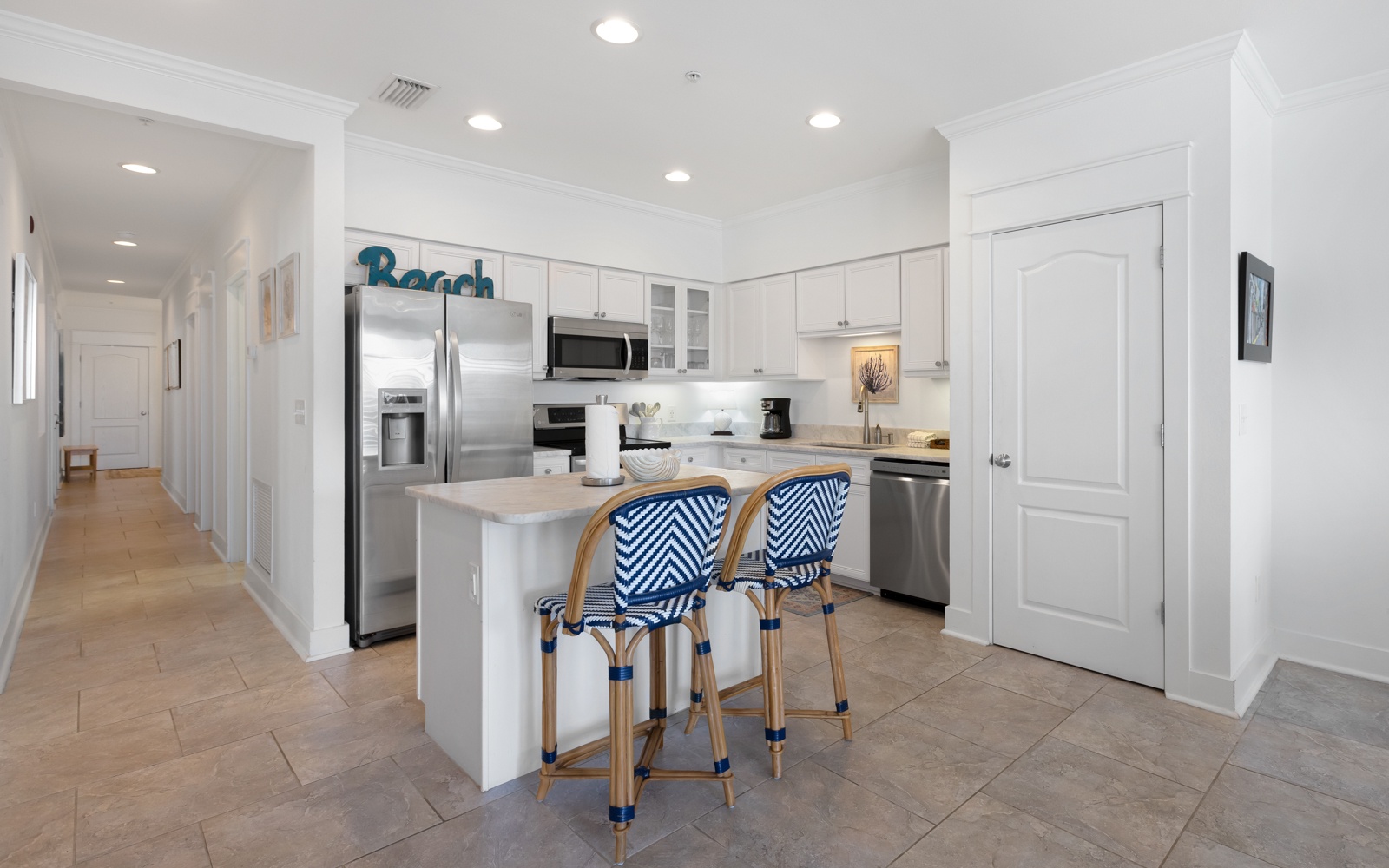 Your coastal-inspired kitchen awaits with crisp white cabinets, stainless appliances, and stylish blue-striped stools perfect for morning coffee.