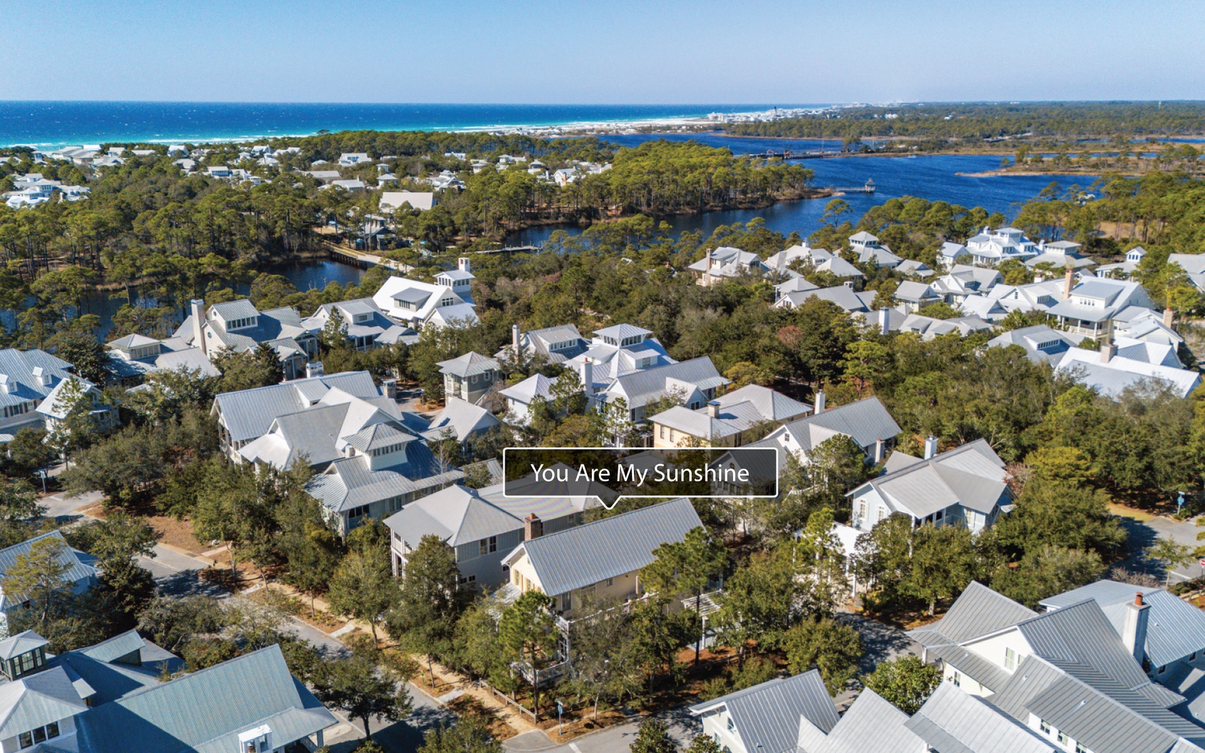 Stunning coastal community with white-roof homes nestled among lush trees, offering waterfront proximity and beach access nearby.